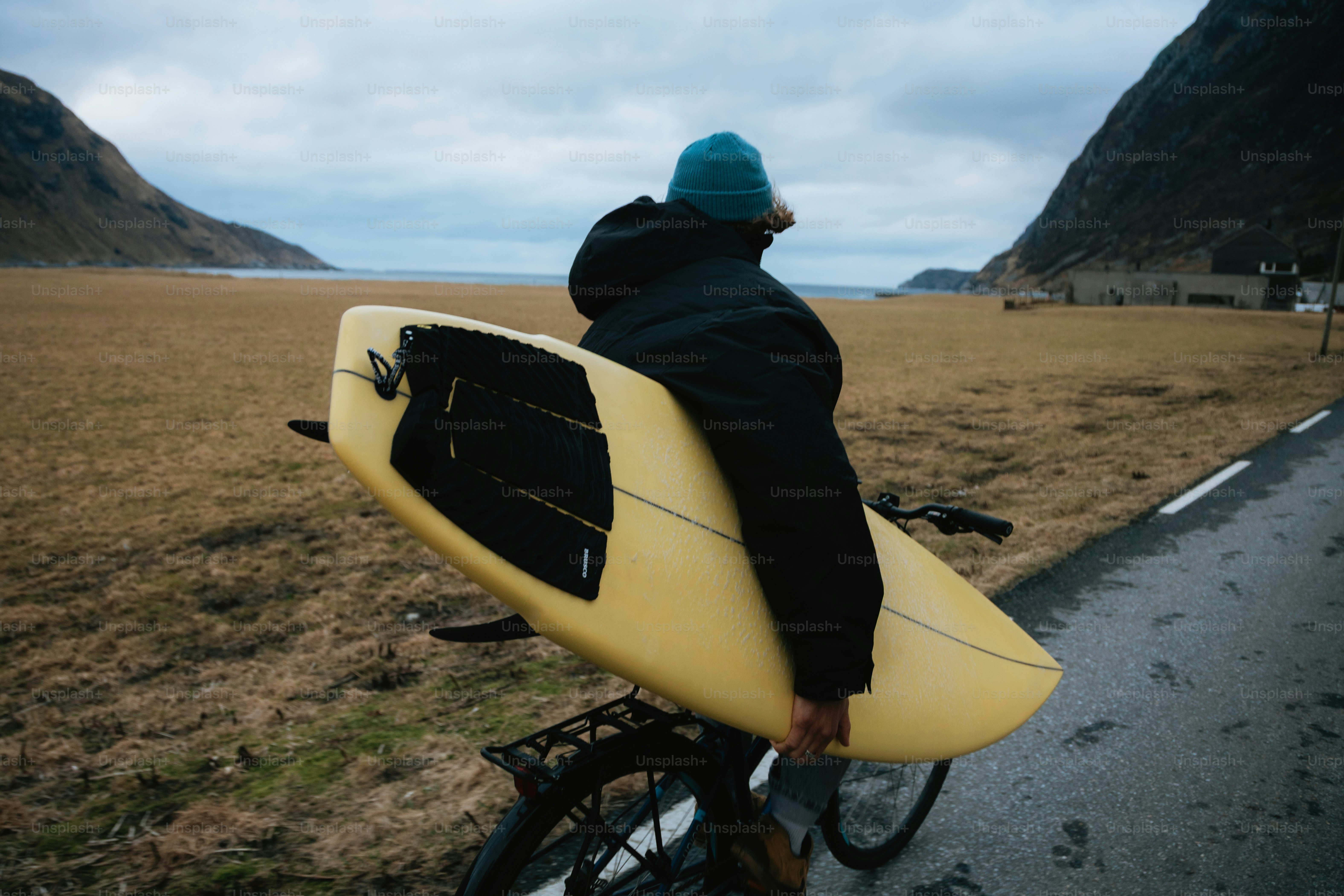 山の近くで黄色いサーフボードを自転車で持っている人。