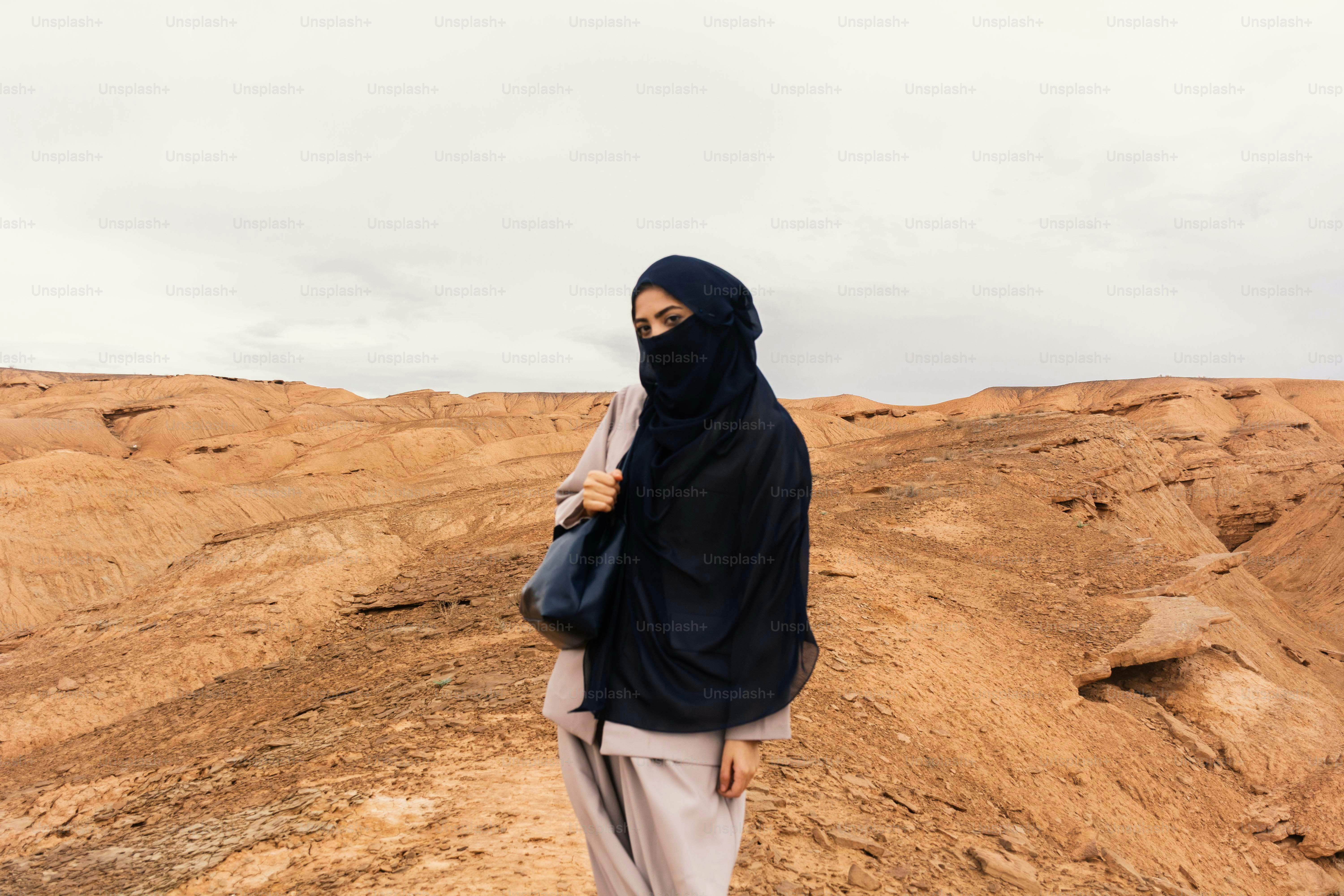 Wanita berhijab hitam berdiri di lanskap gurun