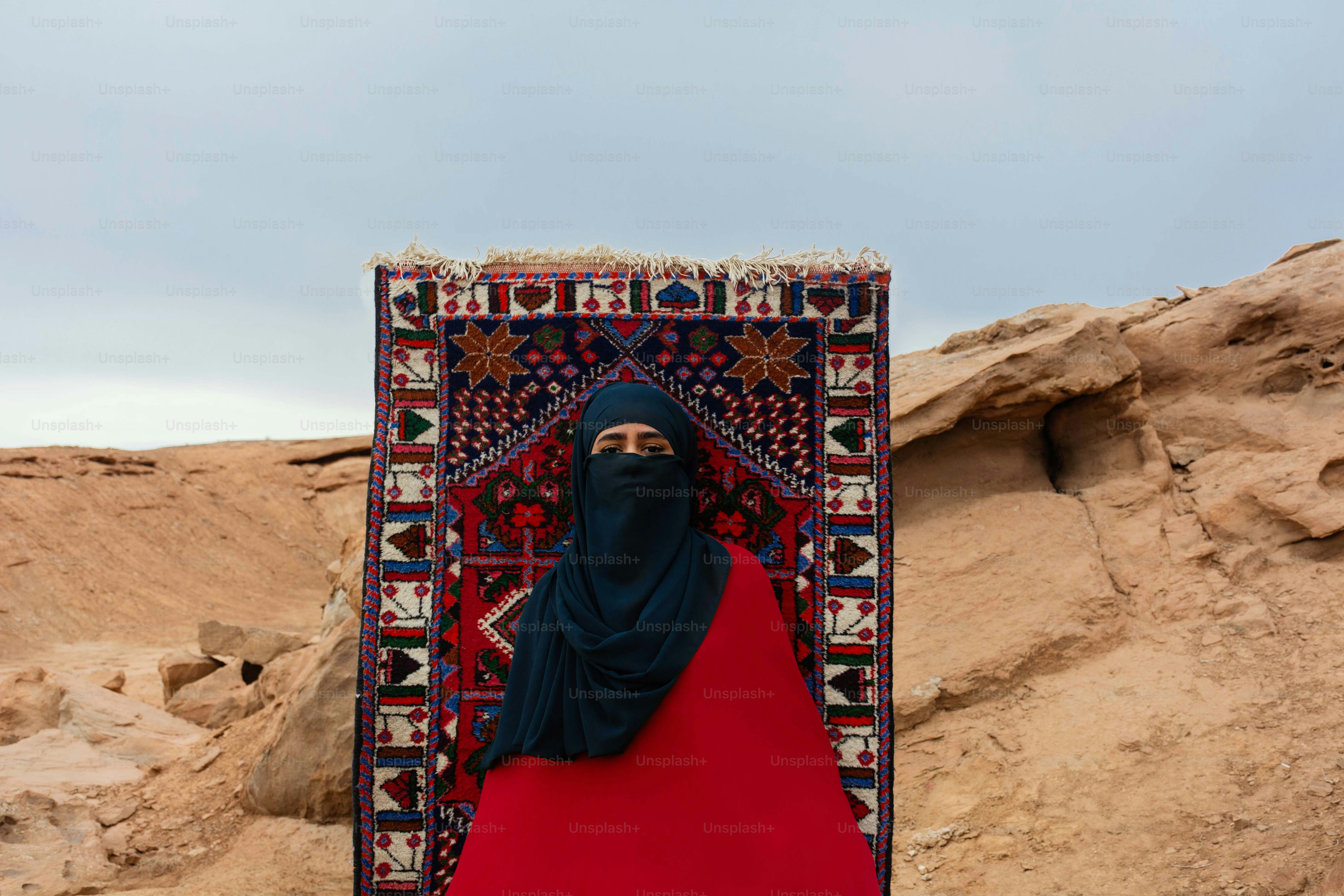 Wanita berpakaian tradisional berdiri di depan permadani di gurun pasir