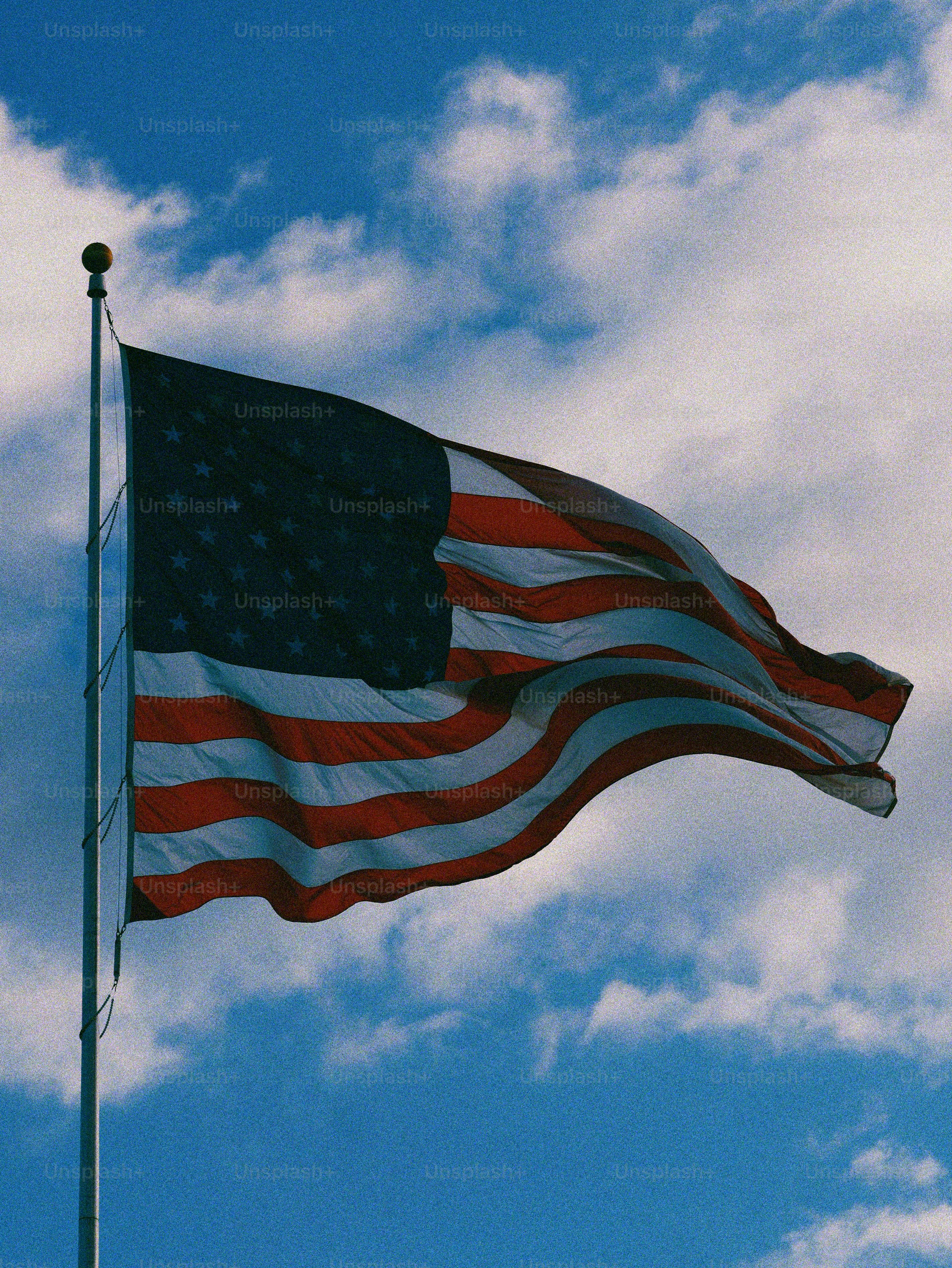 American flag waving on a flagpole against blue sky.