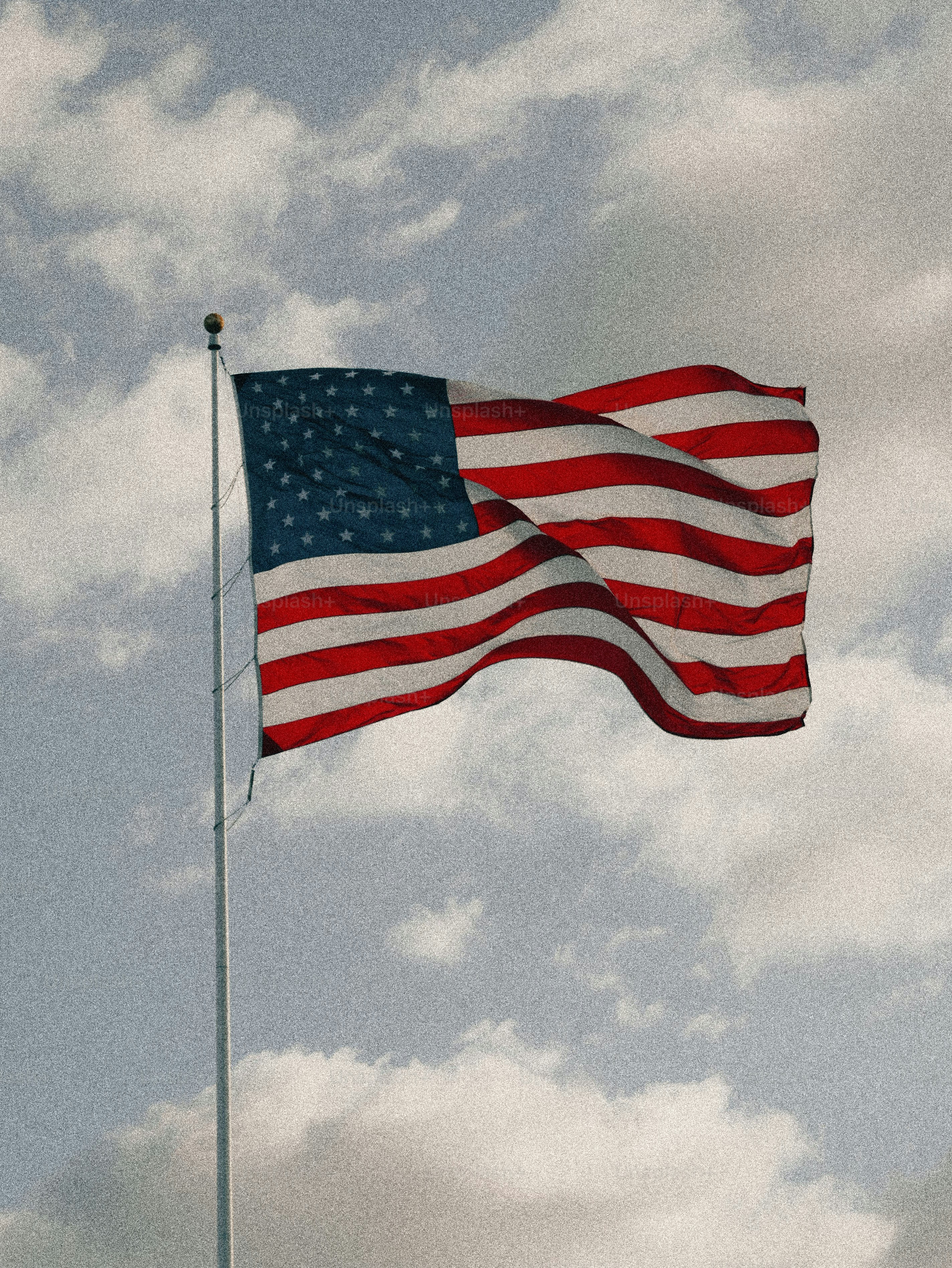 American flag waving on a flagpole against a cloudy sky.