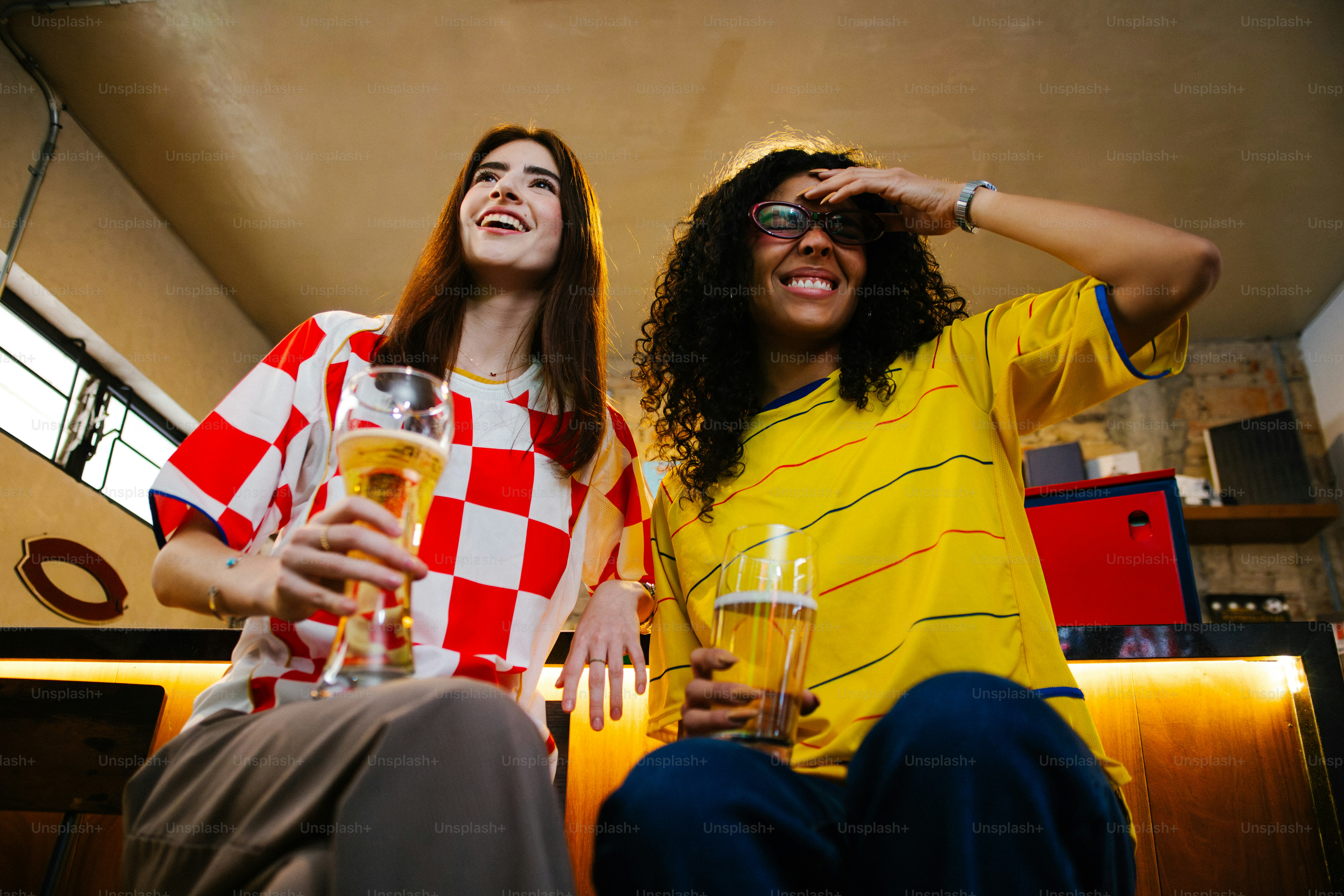 Due donne in maglie che tengono birra in mano e guardano una partita