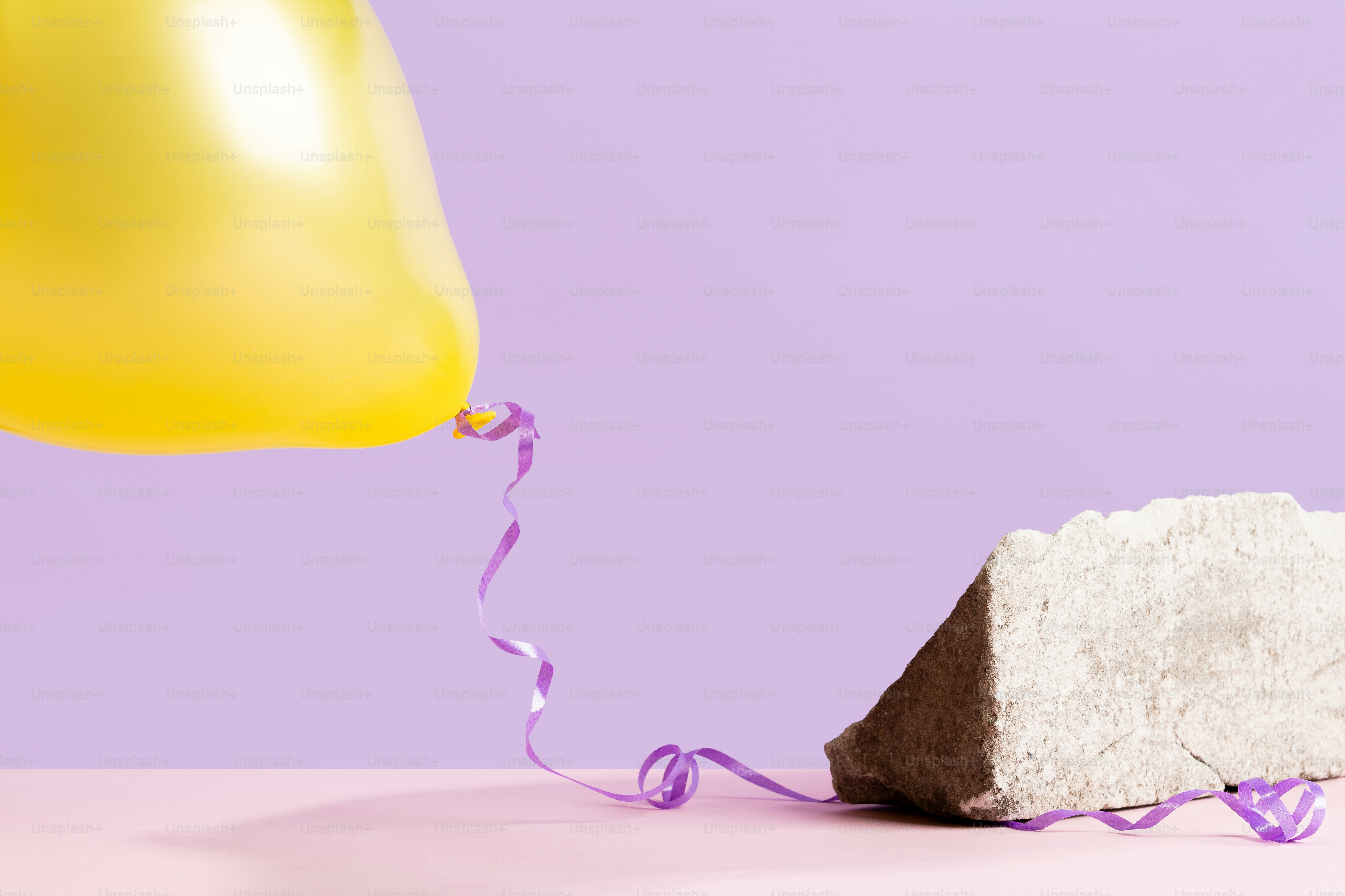 Yellow balloon with purple ribbon near rock
