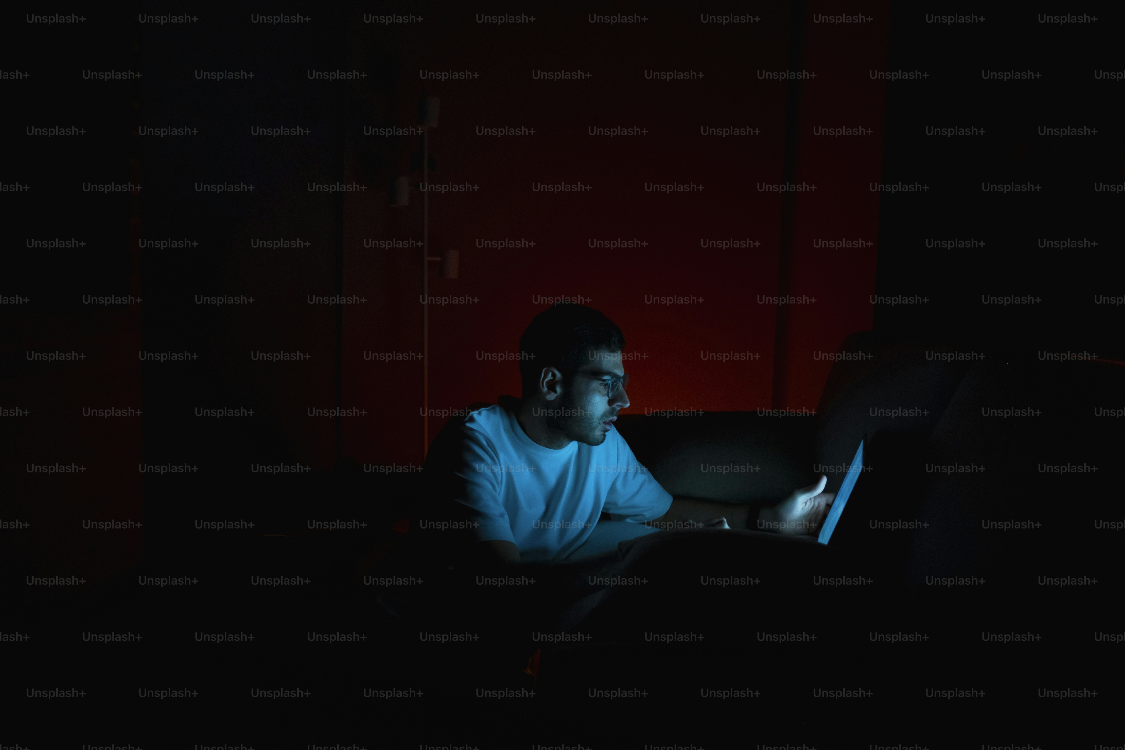 Man illuminated by a laptop screen in dark room.
