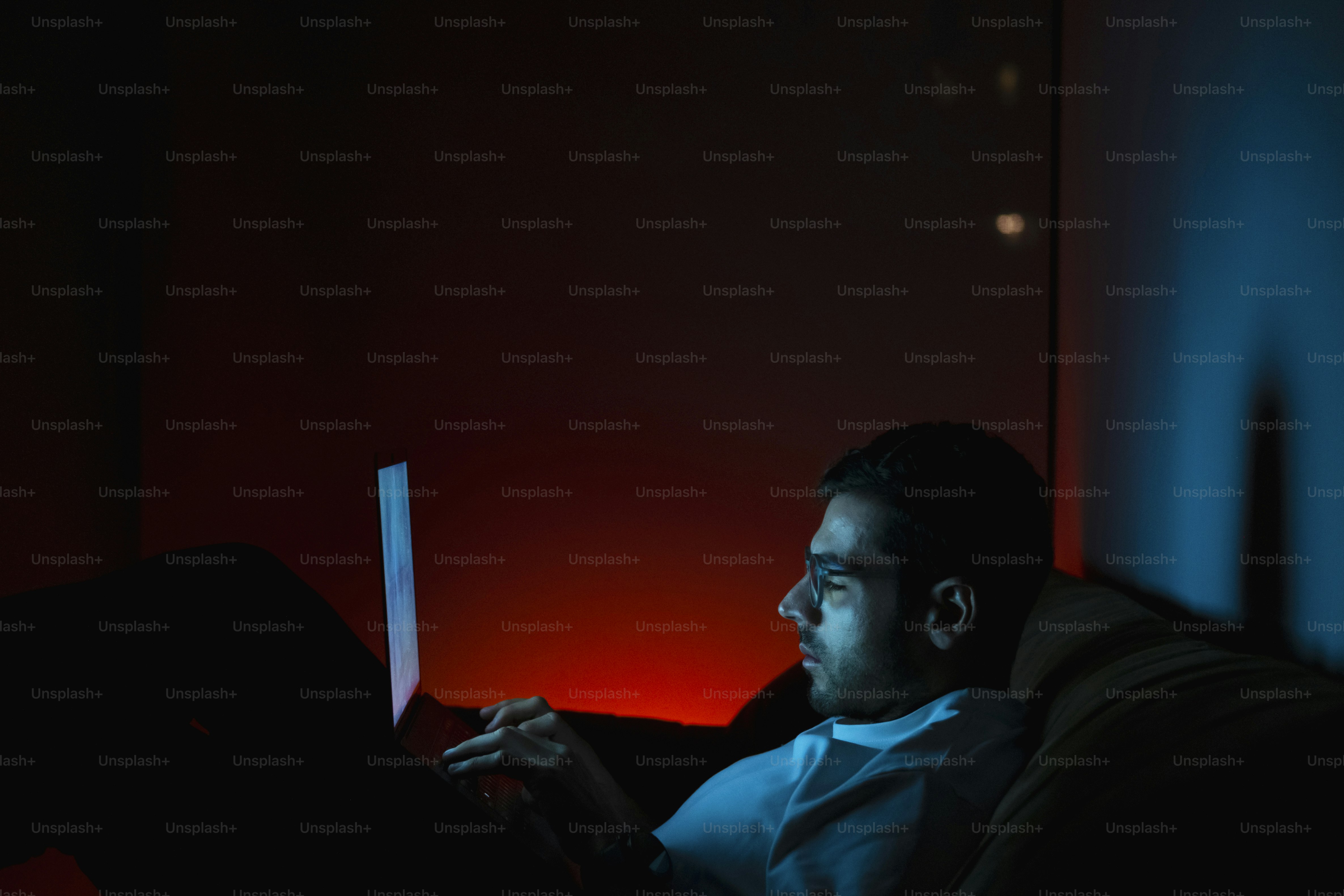 Man illuminated by laptop screen in dark room