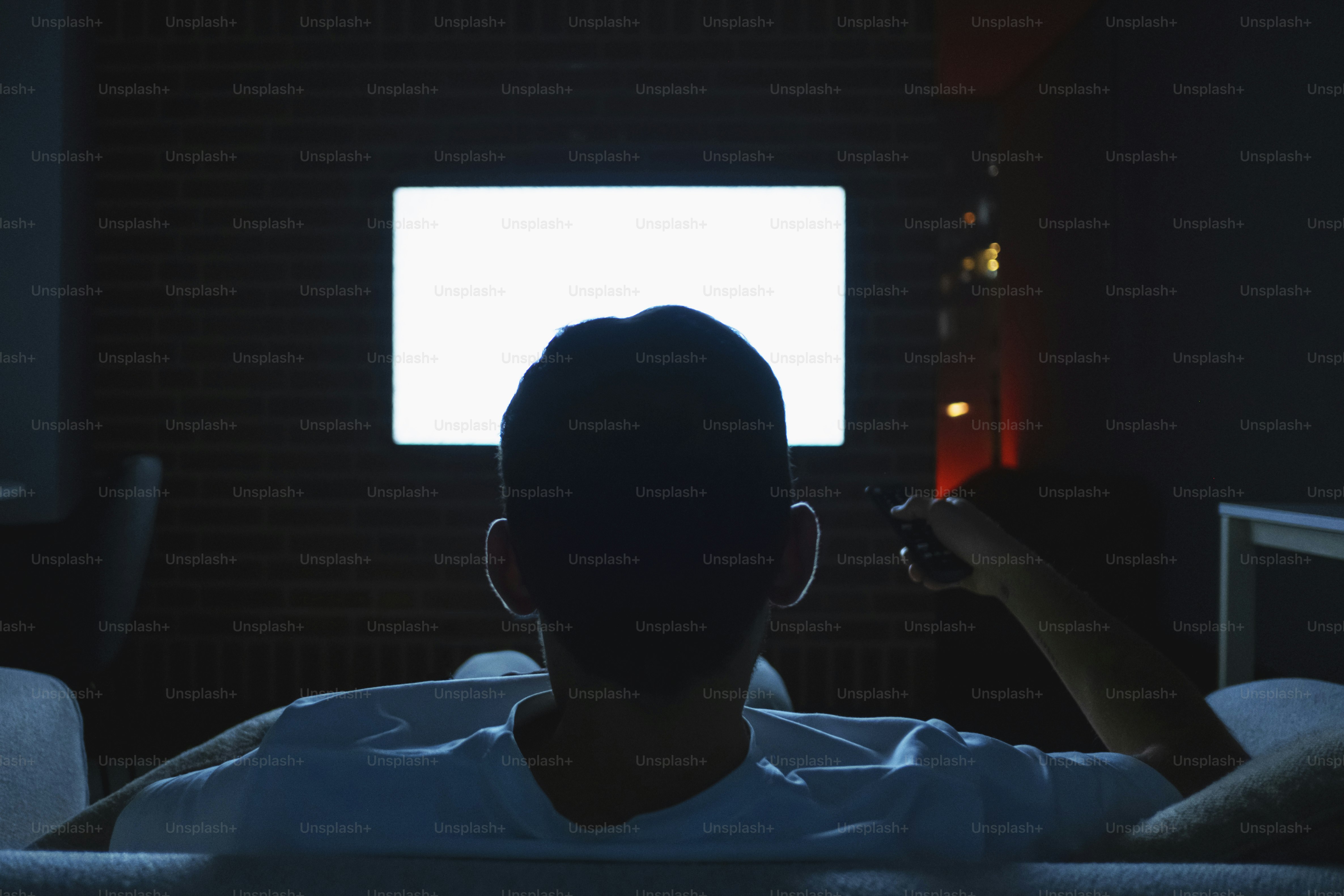 Man watching a blank television screen in a dark room.