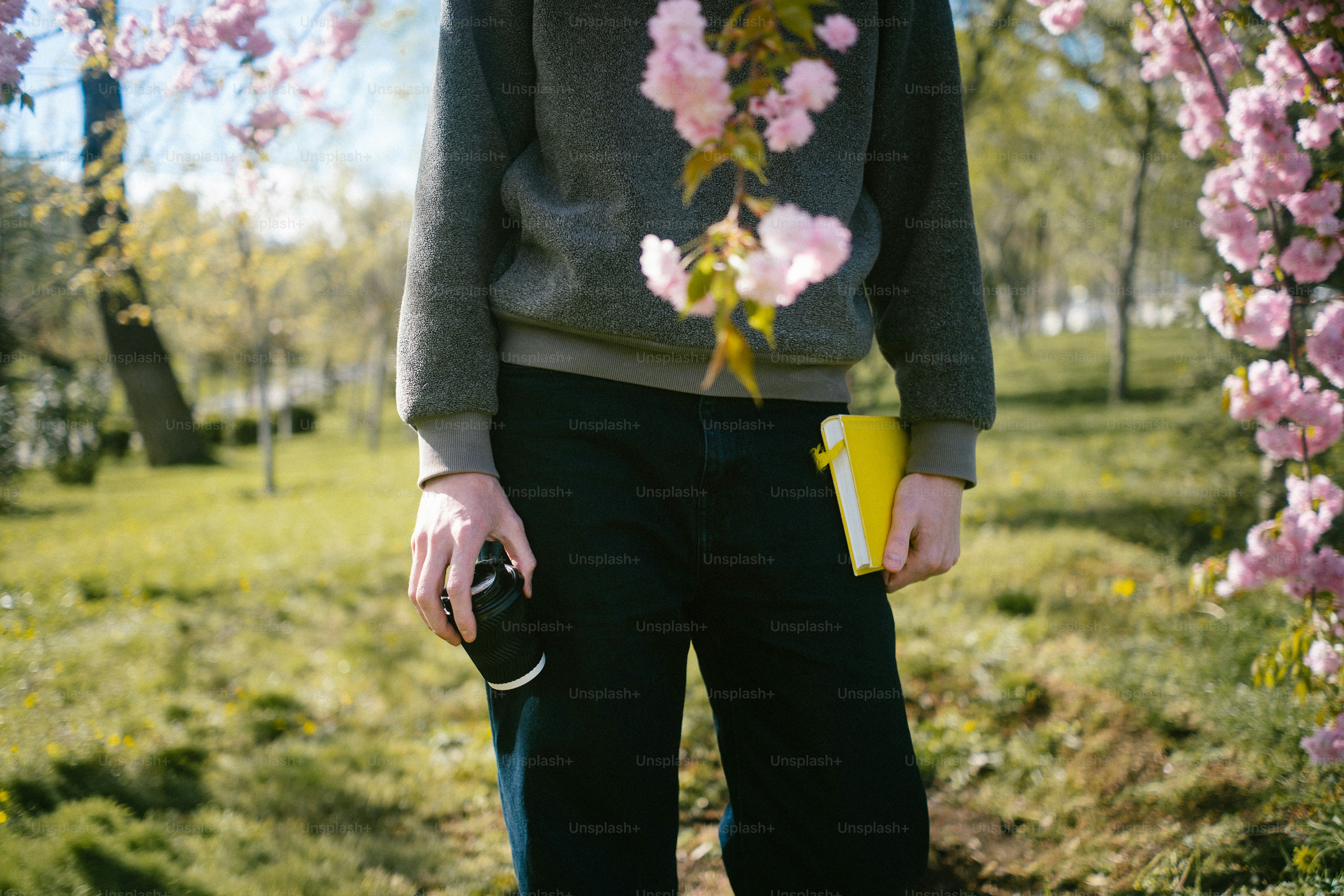 Person holding coffee cup and book among cherry blossoms