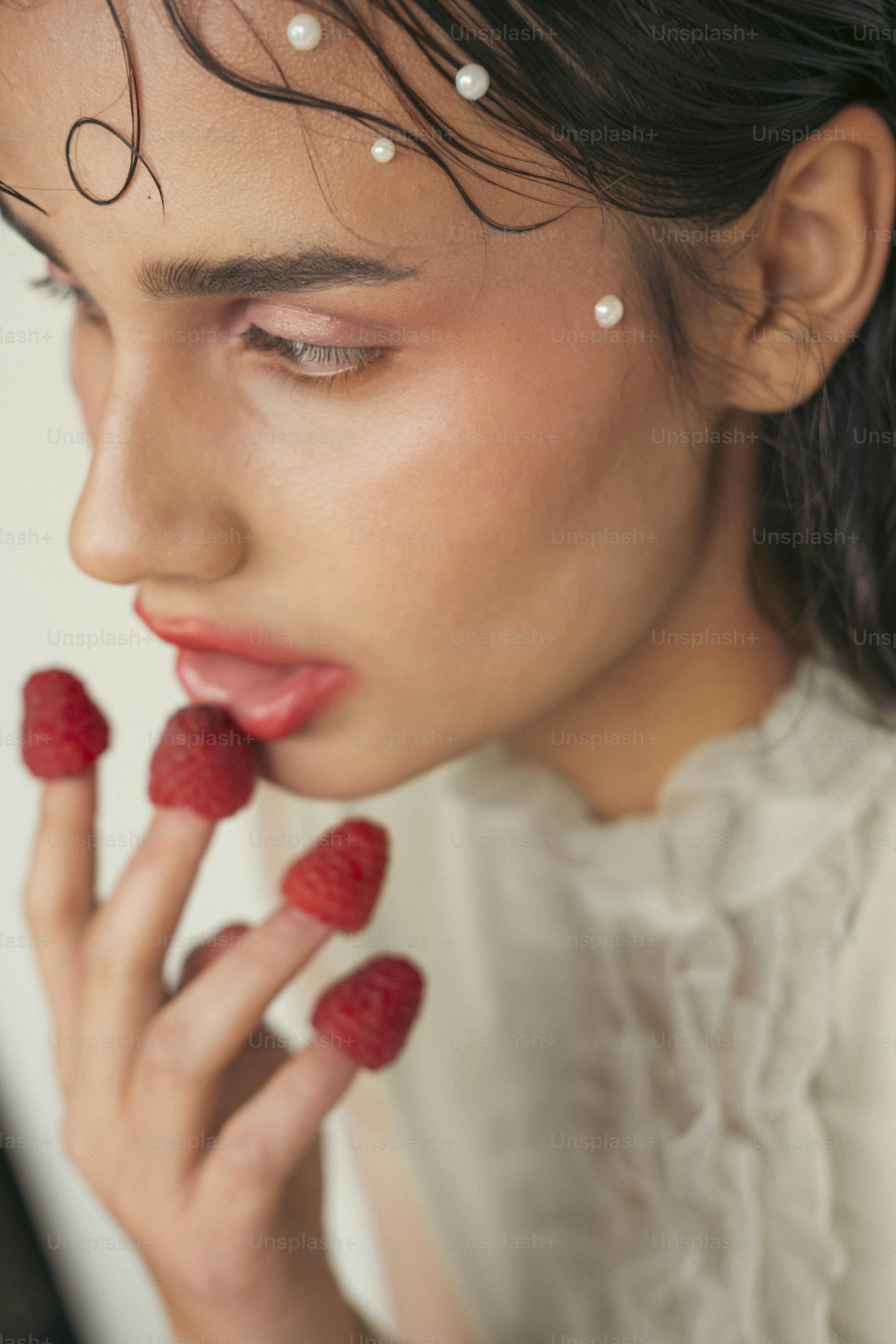 Wanita dengan raspberry di jari dan mutiara di wajah
