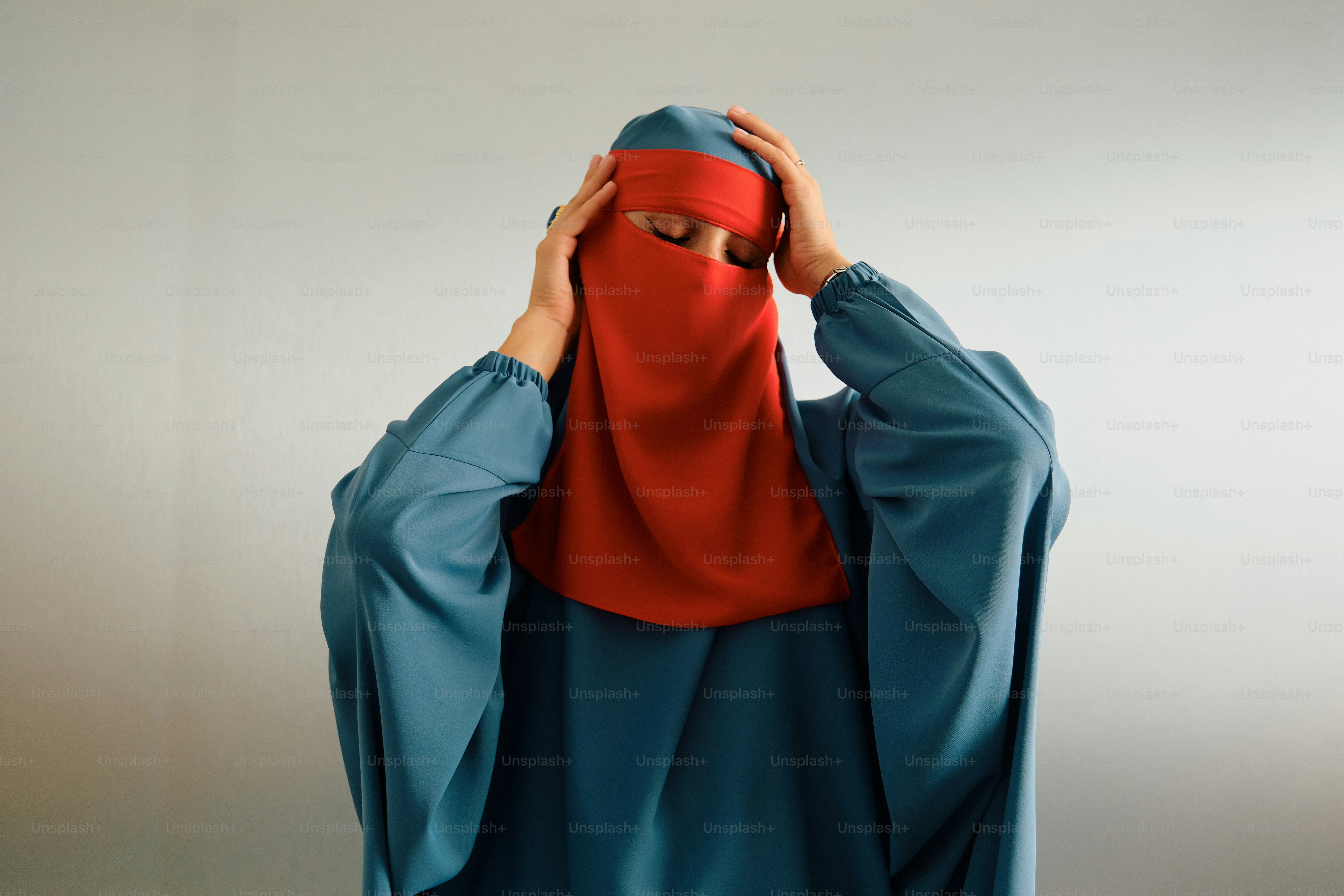Wanita berbaju abaya biru dan niqab merah memegang kepala