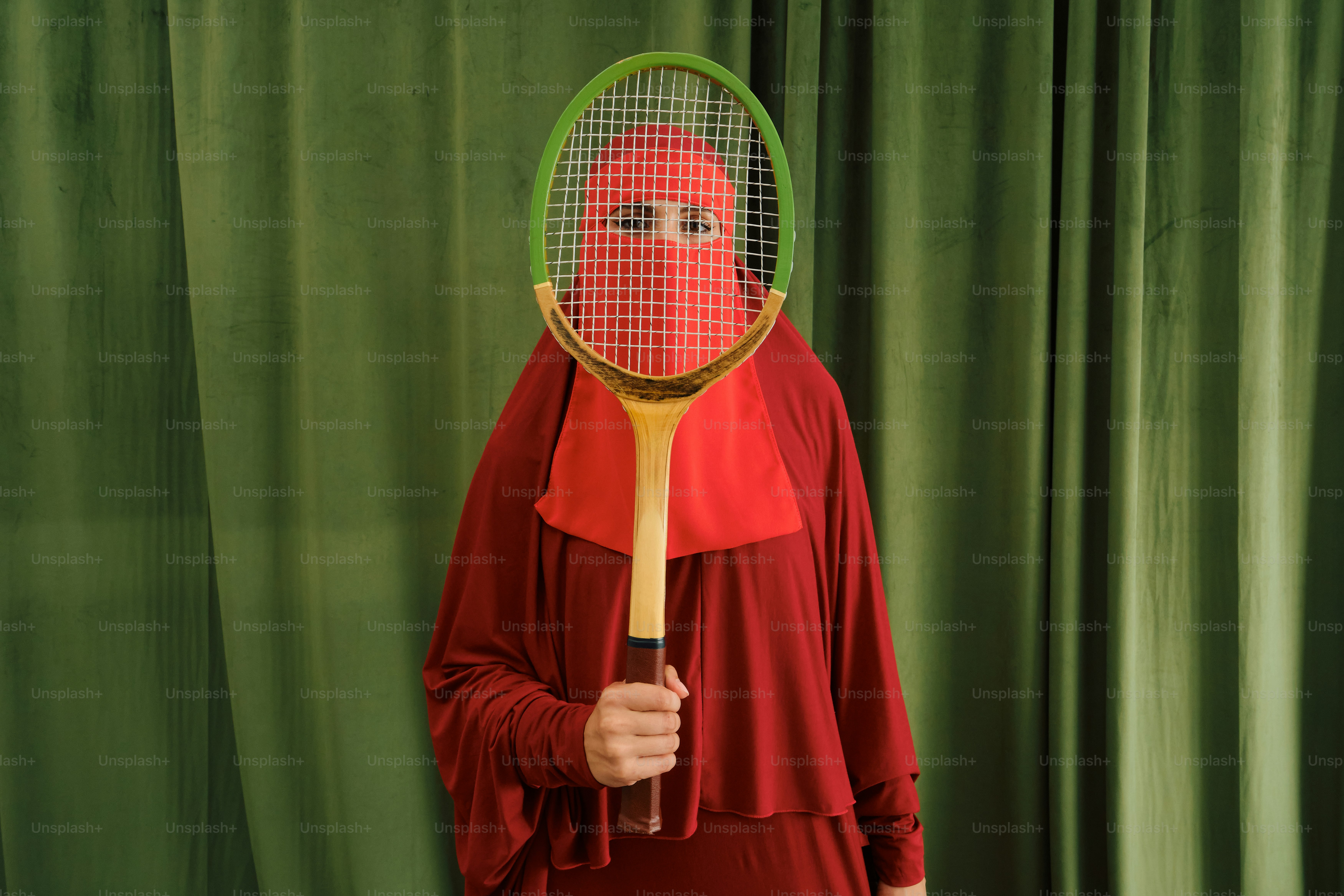 Orang berbaju merah menutupi wajah dengan raket tenis