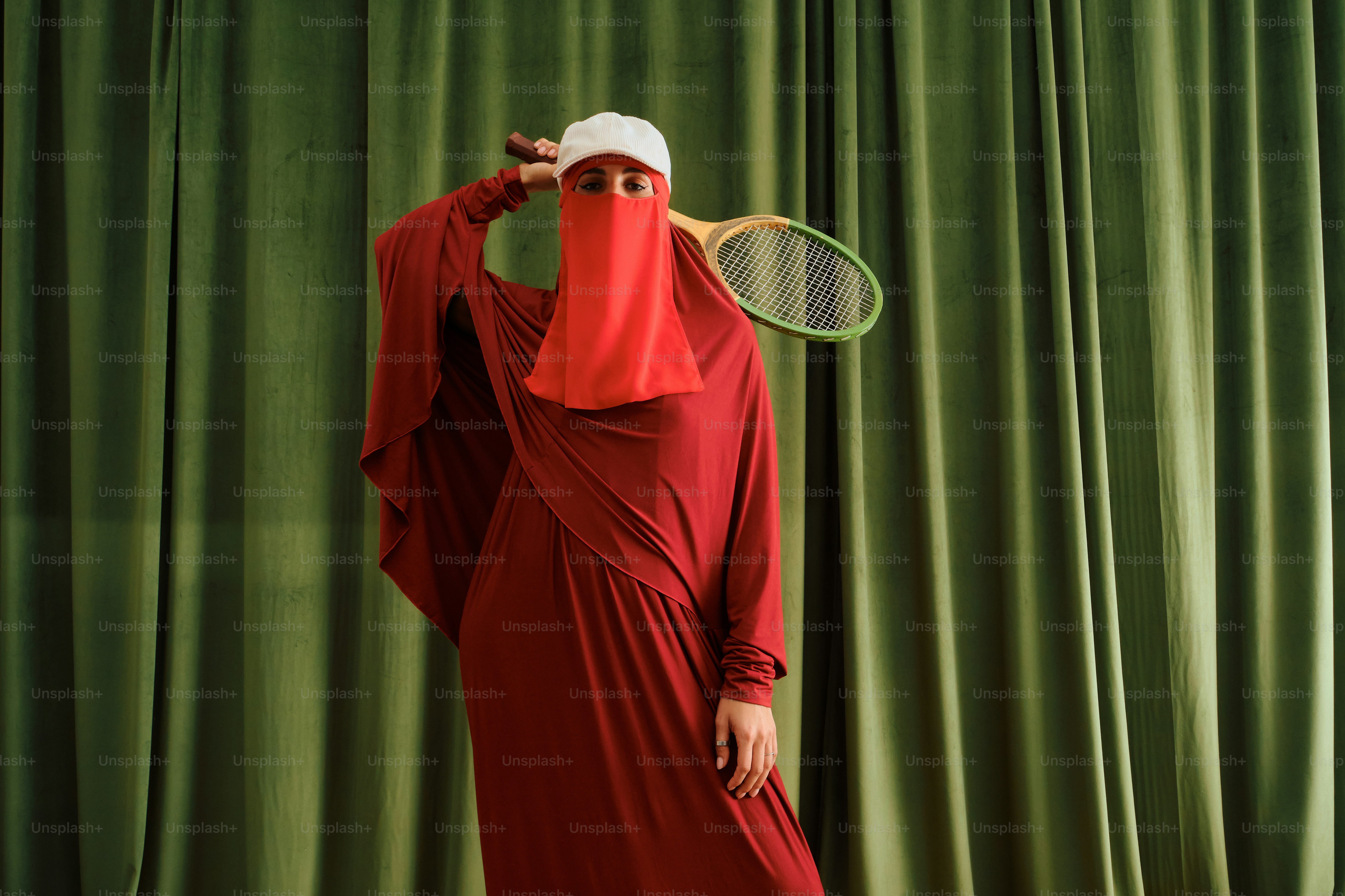 Wanita berpakaian merah dan niqab memegang raket tenis.