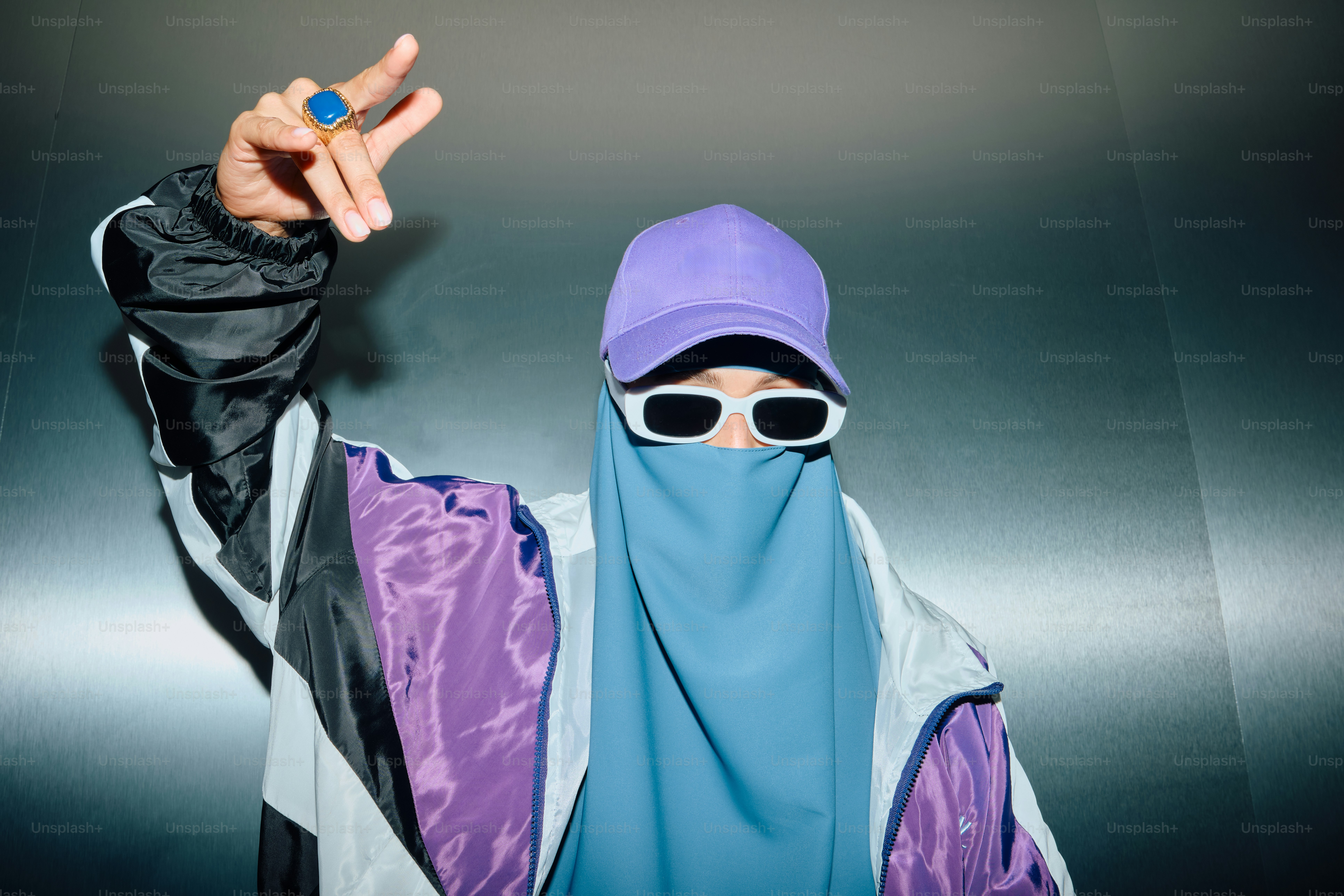 Orang dengan kacamata hitam dan topi ungu memberi isyarat dengan tangan.