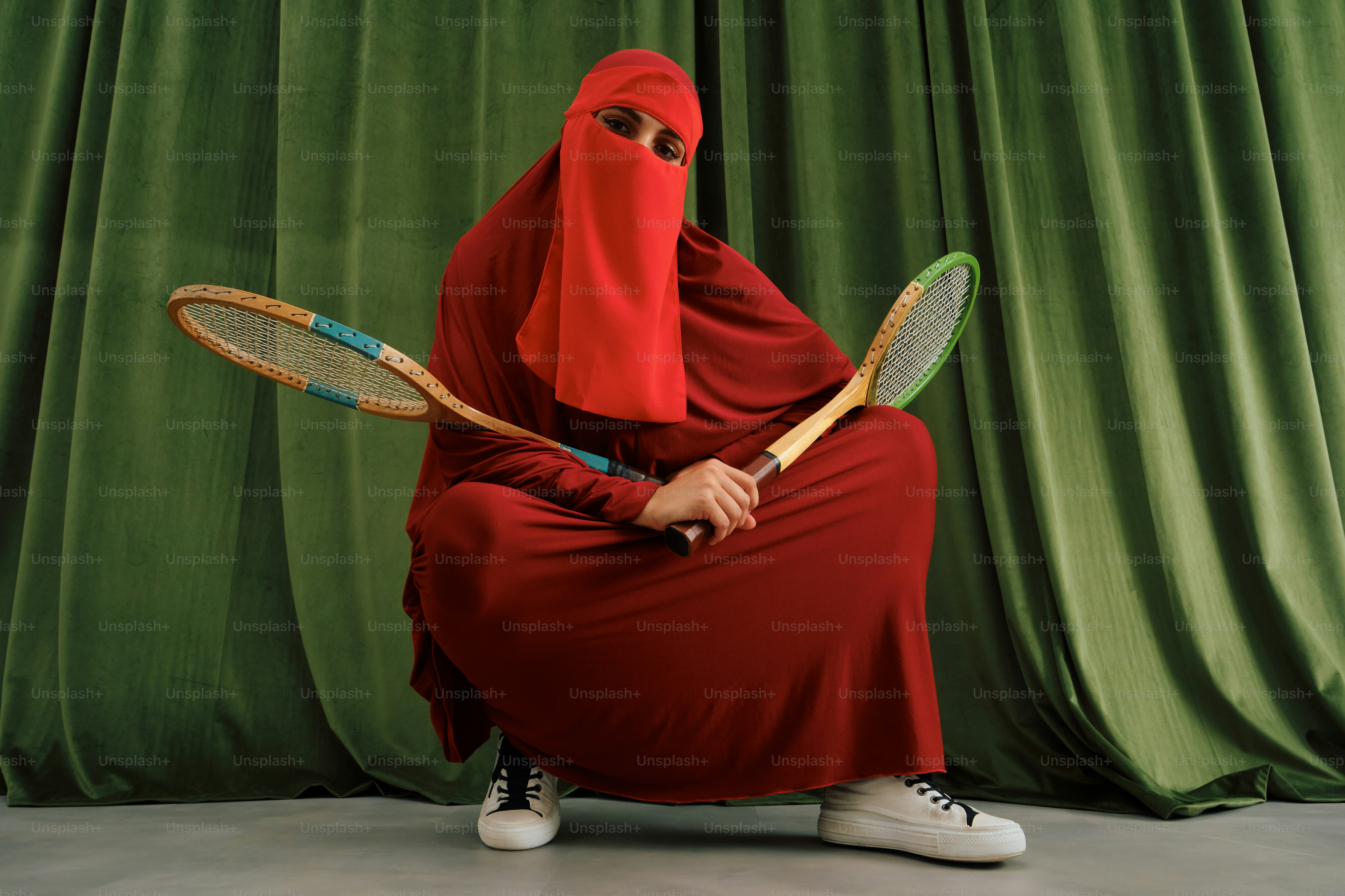 Orang dengan niqab merah memegang dua raket tenis vintage