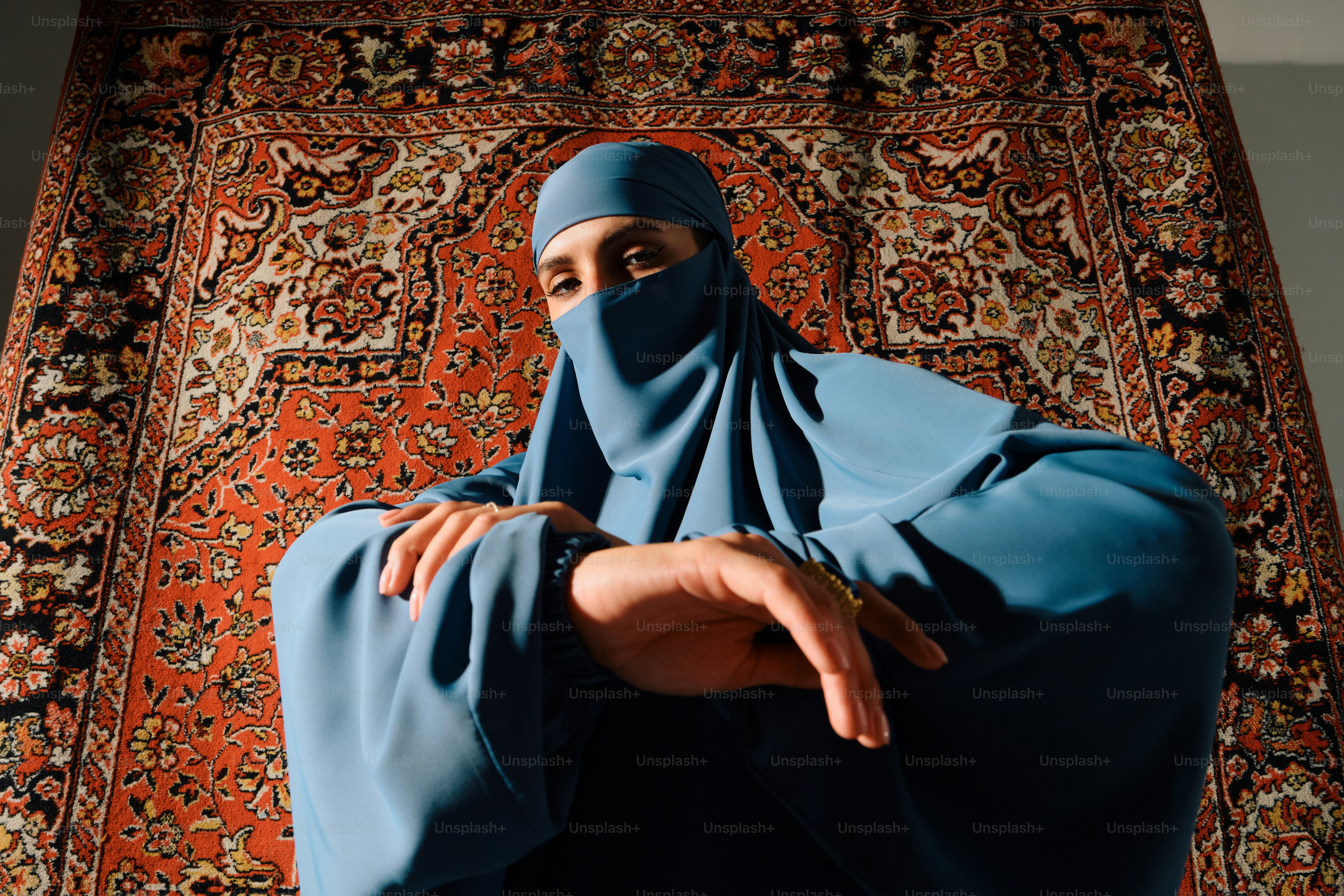 Wanita berjilbab biru dan niqab duduk di depan karpet