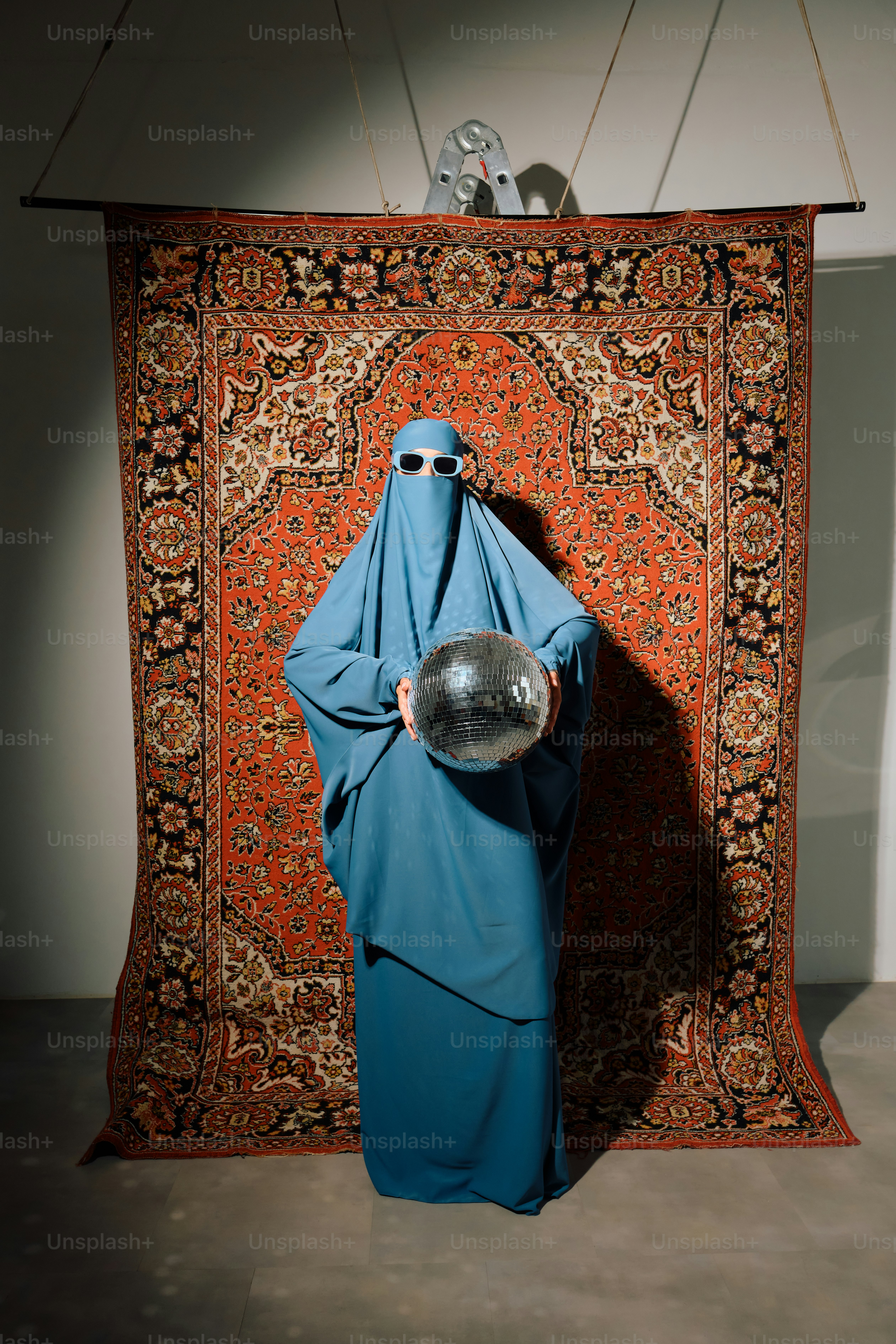 Persona in burqa blu tiene una palla da discoteca davanti al tappeto
