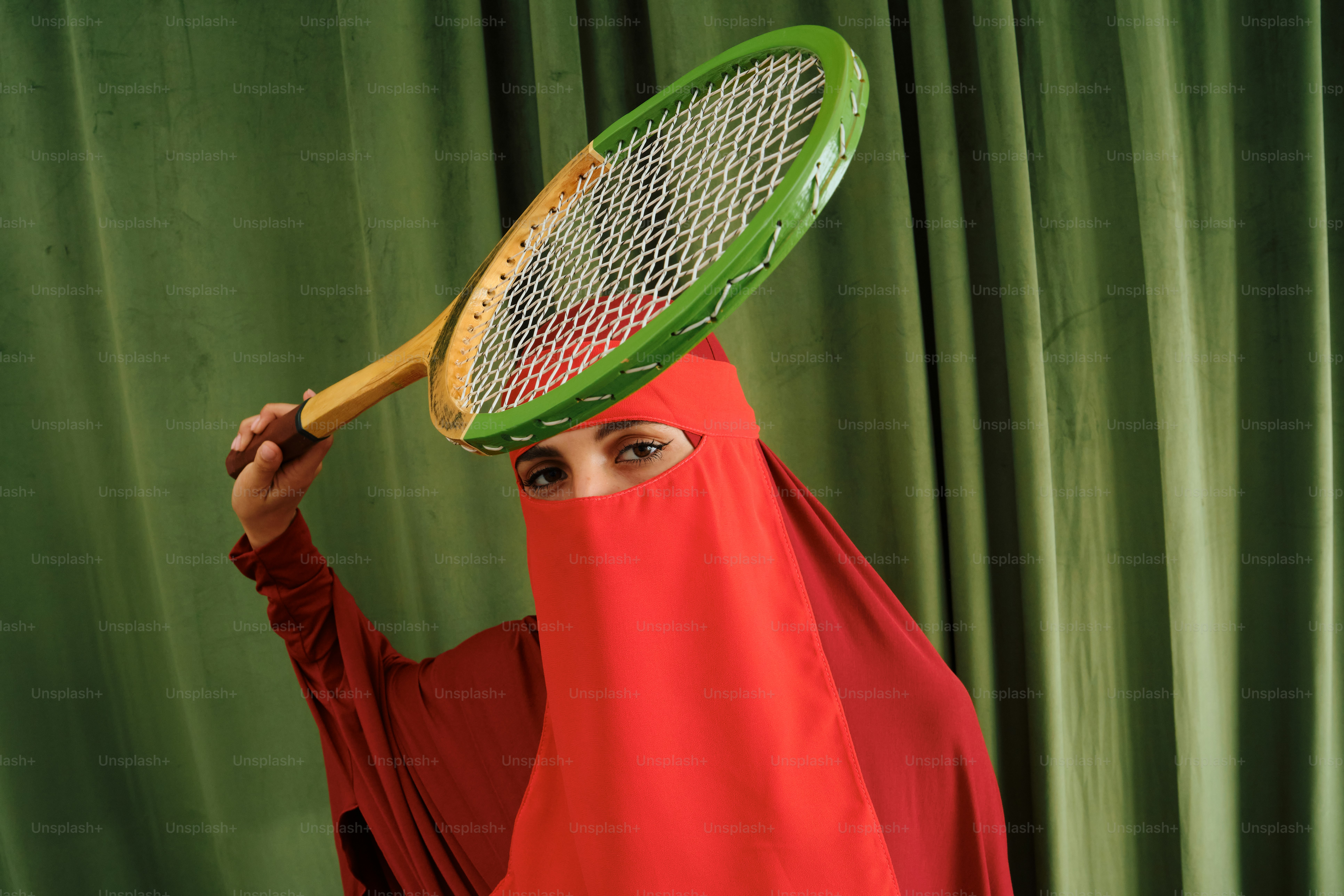 Wanita berniqab merah memegang raket tenis di atas kepala