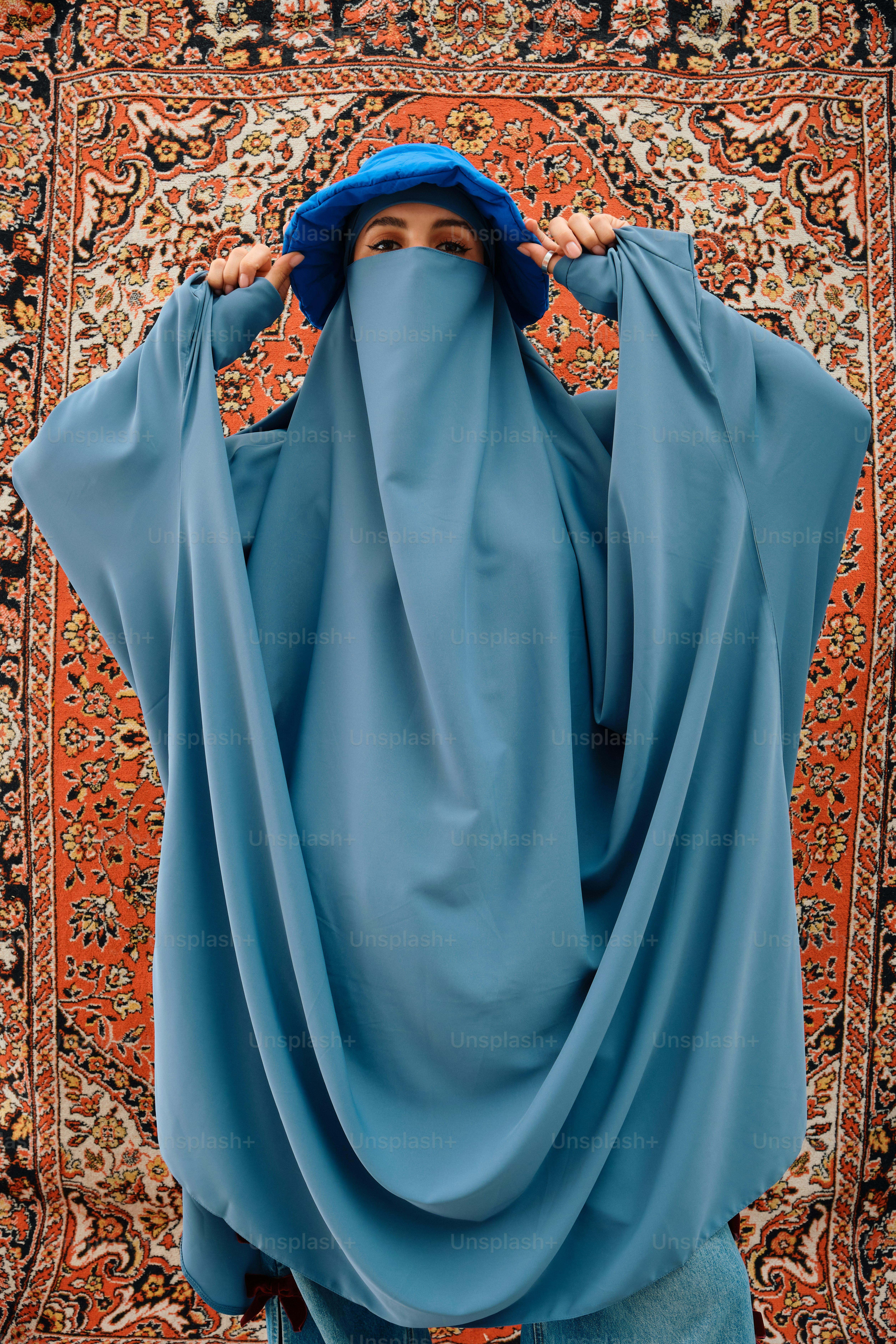 Wanita berjilbab biru dan burqa berdiri di atas karpet
