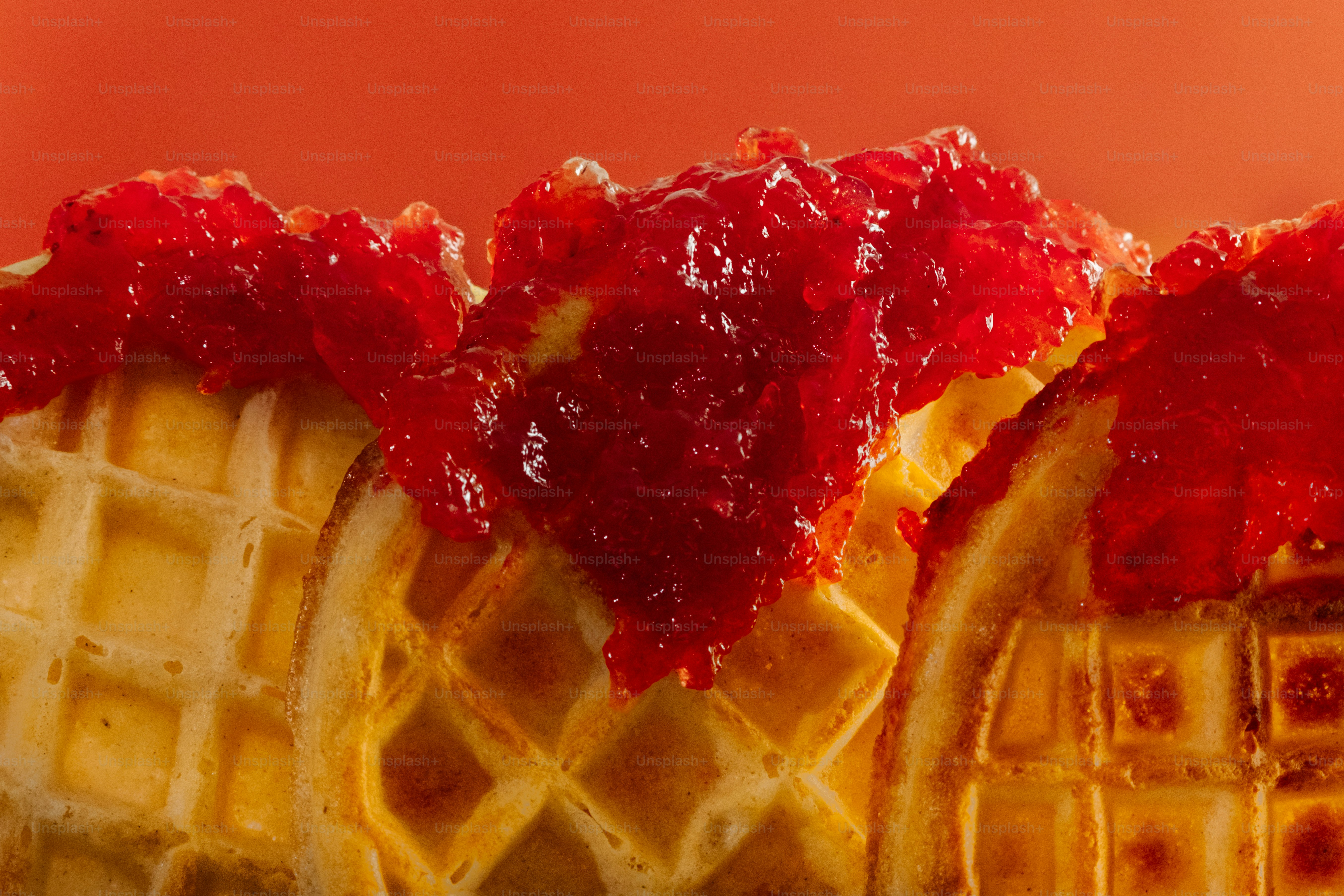 Três waffles cobertos com geleia vermelha sobre fundo laranja