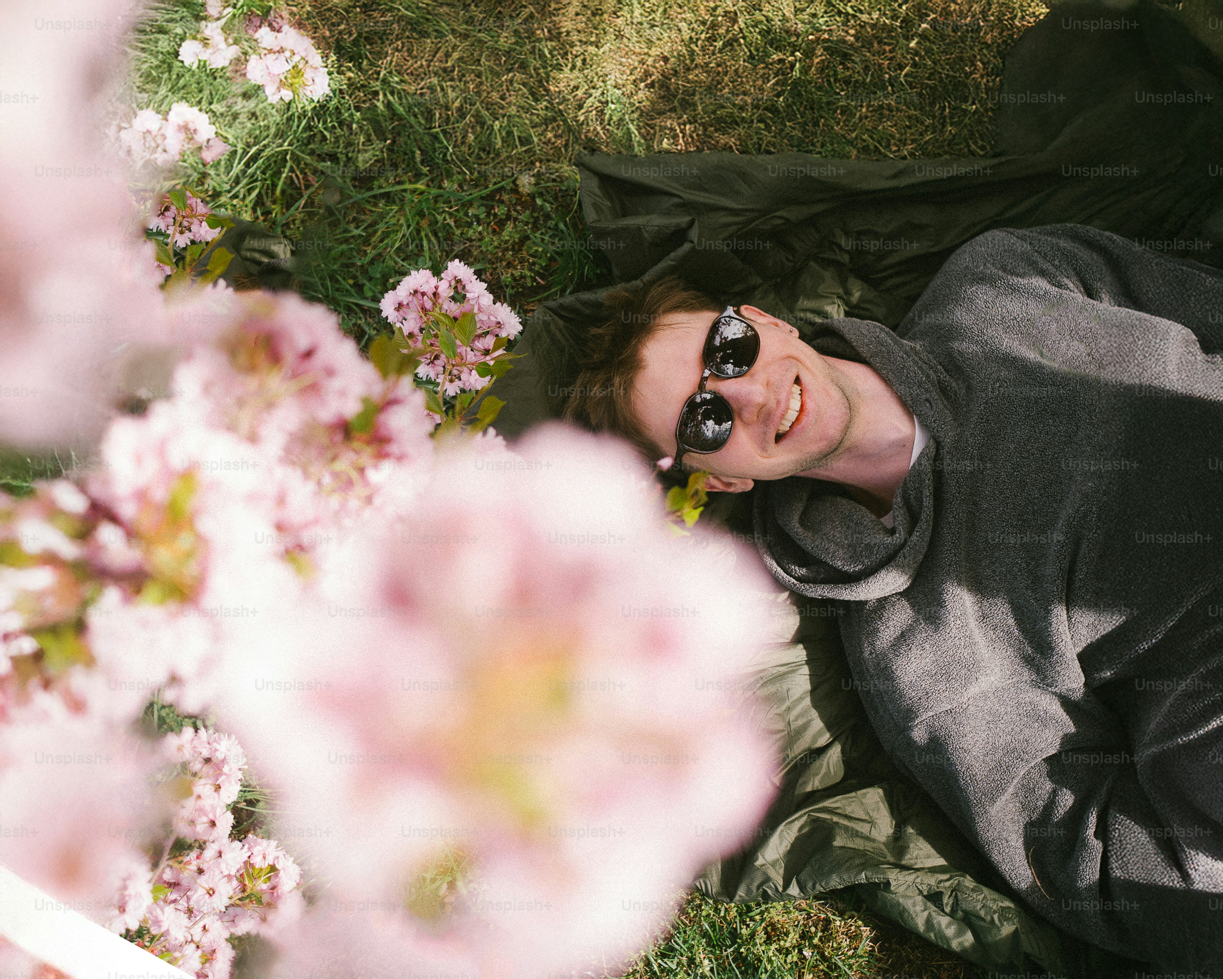 Young man smiling lying in grass near cherry blossoms