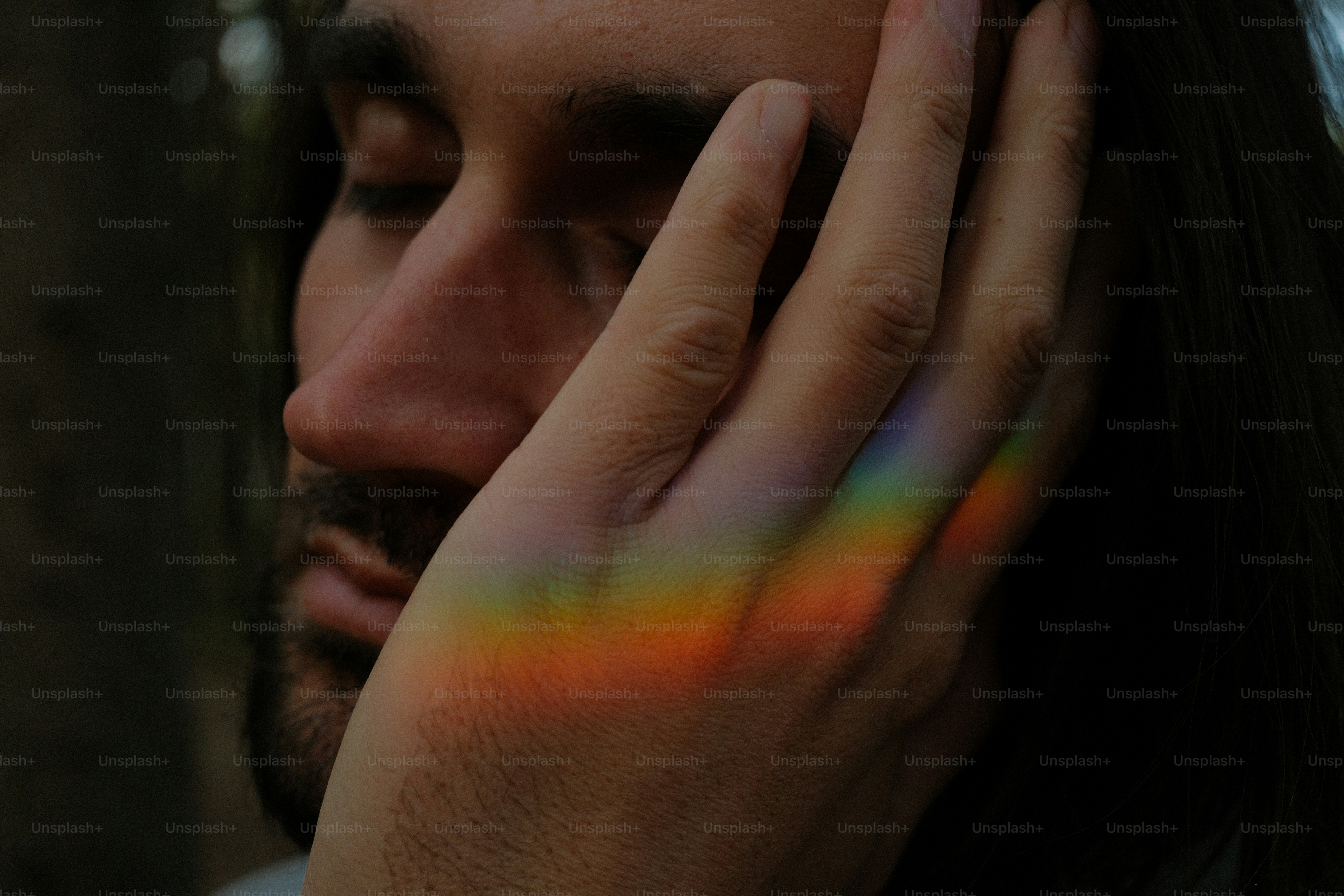 Man's face with rainbow light on hand