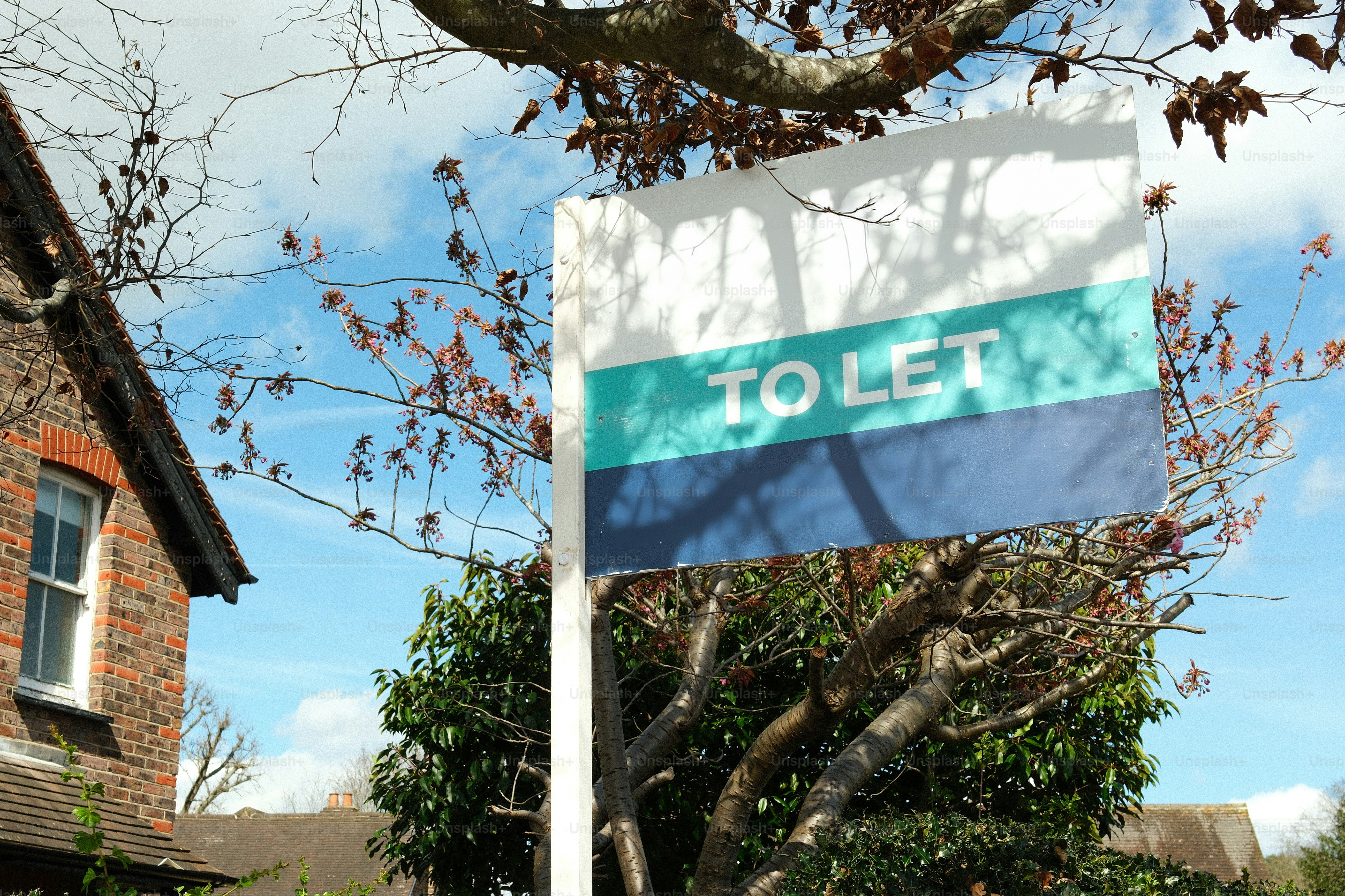 Un cartel de 'alquilar' delante de una casa de ladrillo.