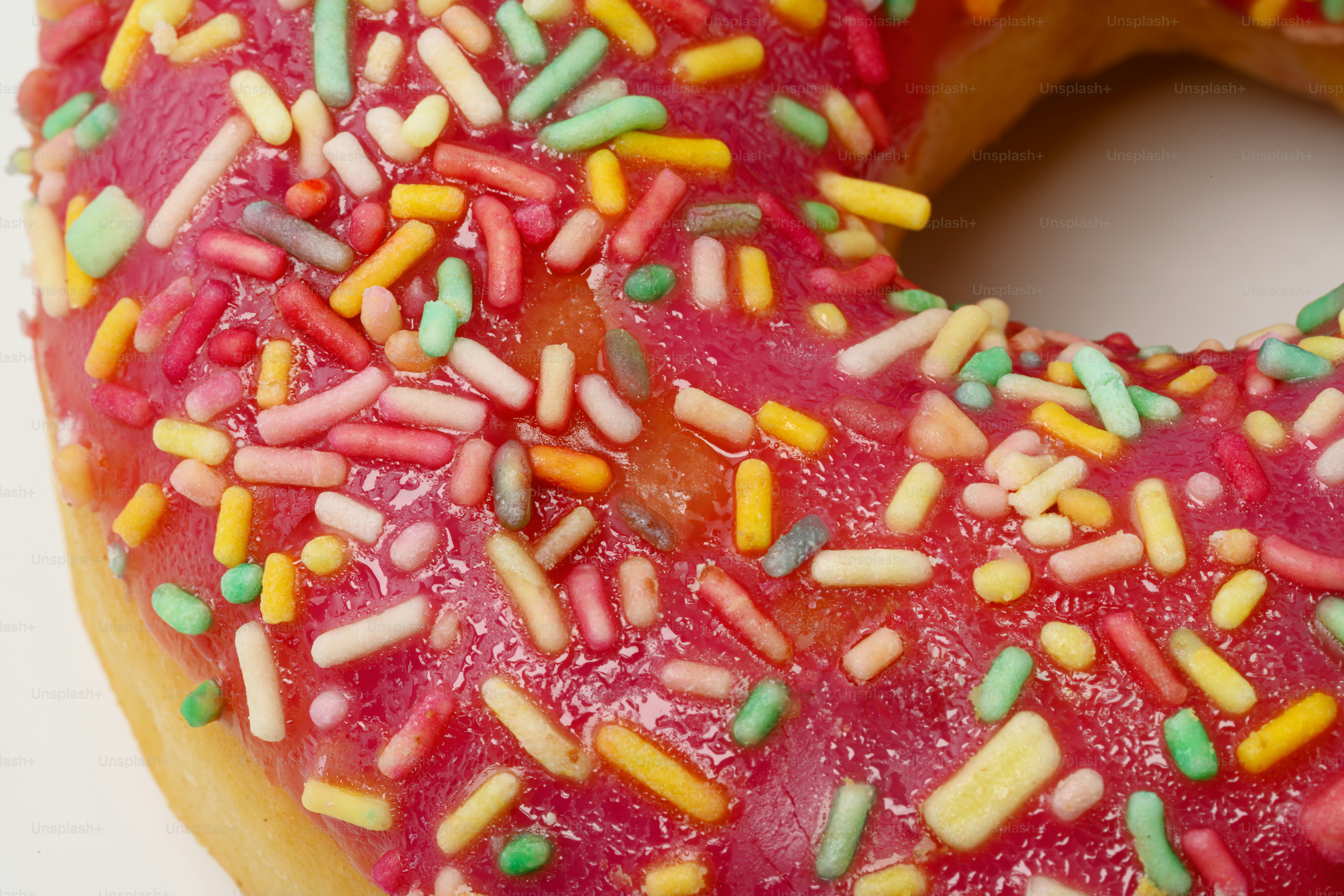 Nahaufnahme eines rosa glasierten Donuts mit bunten Streuseln