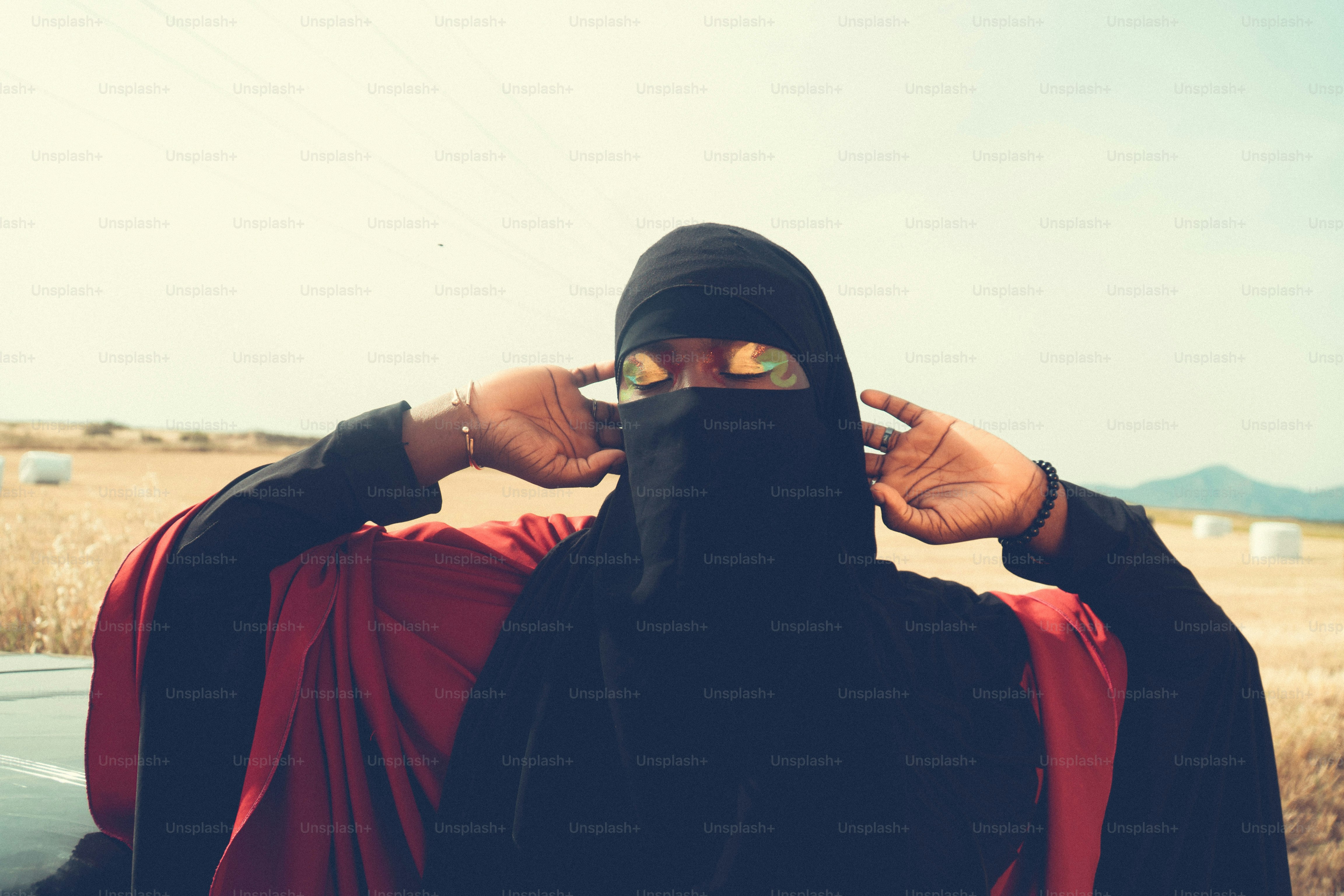 Wanita berjilbab hitam dan kacamata hitam menyesuaikan penutup kepalanya