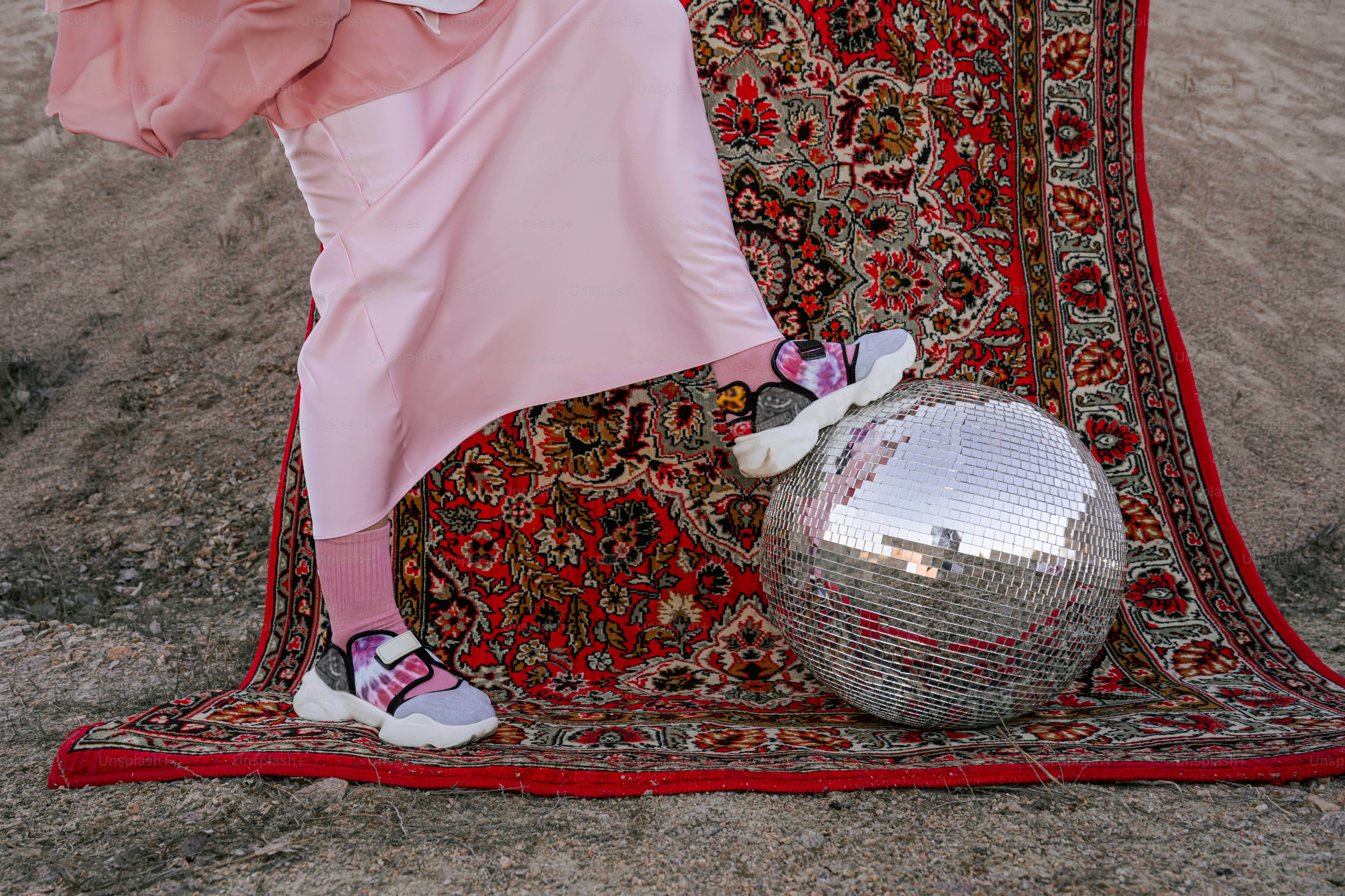 Pink-clad person with sneakers near disco ball on rug