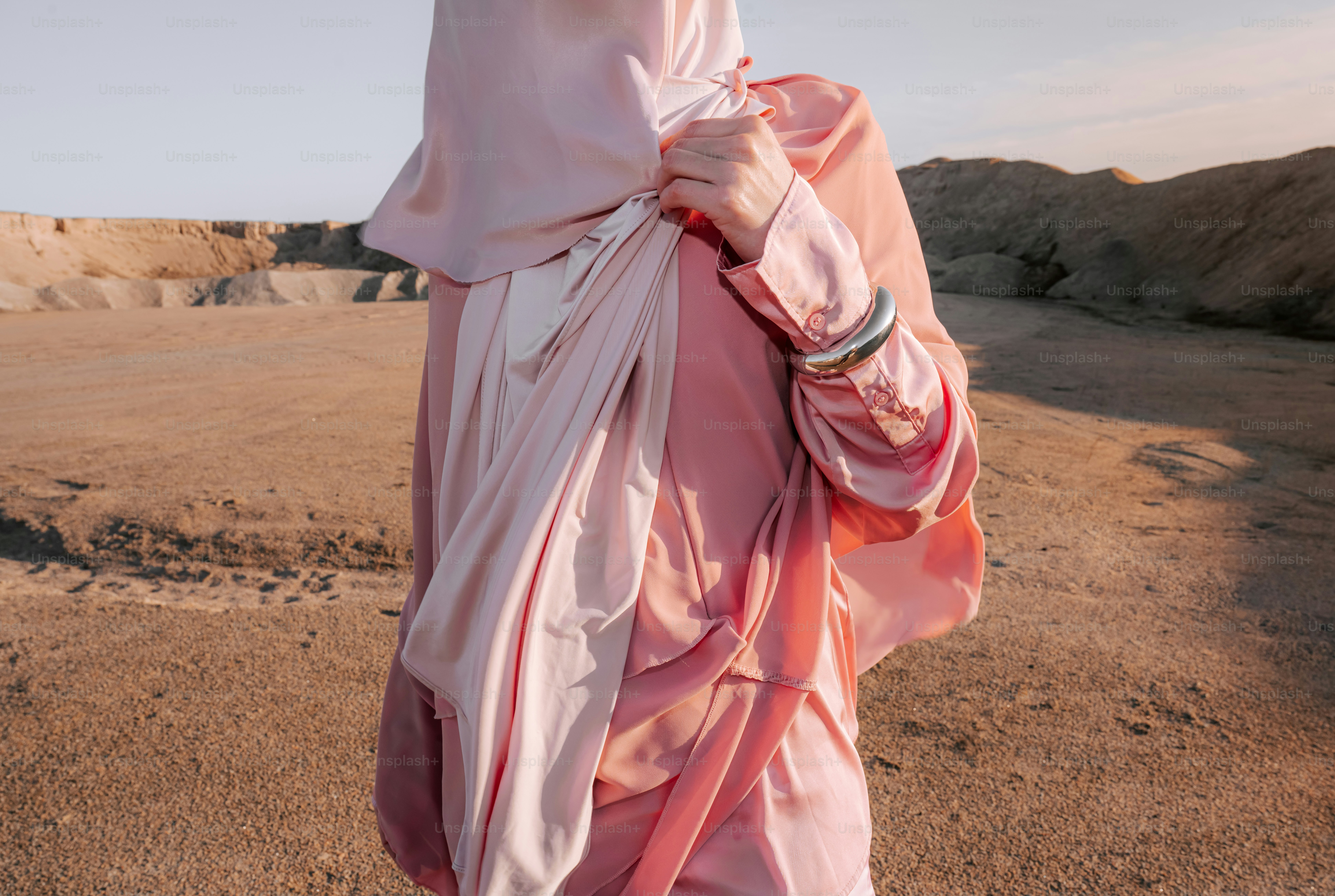 Woman in pink hijab and dress in desert landscape