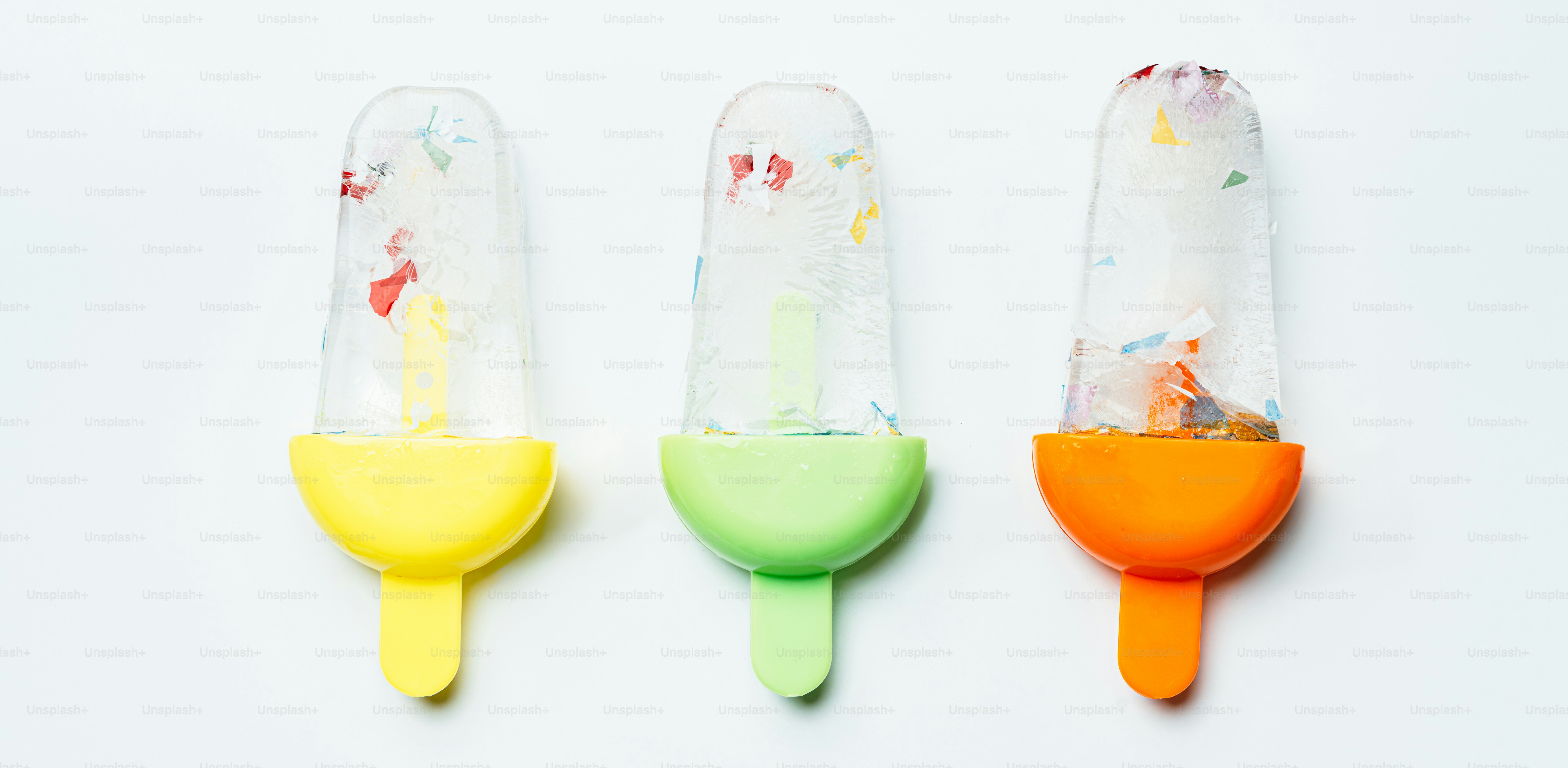 Three popsicles with colorful sprinkles on white background