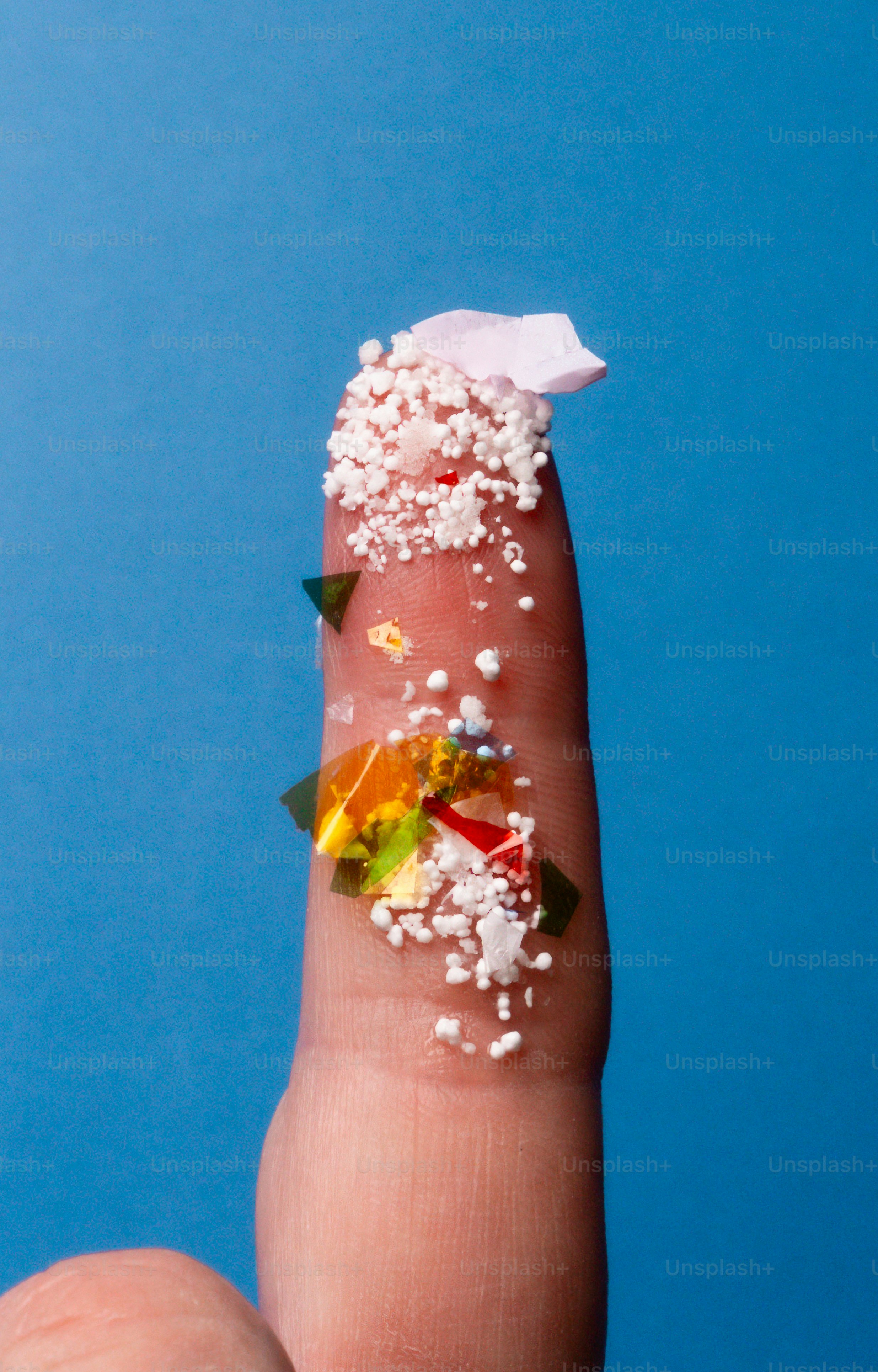 A finger covered in small white beads and colorful fragments.