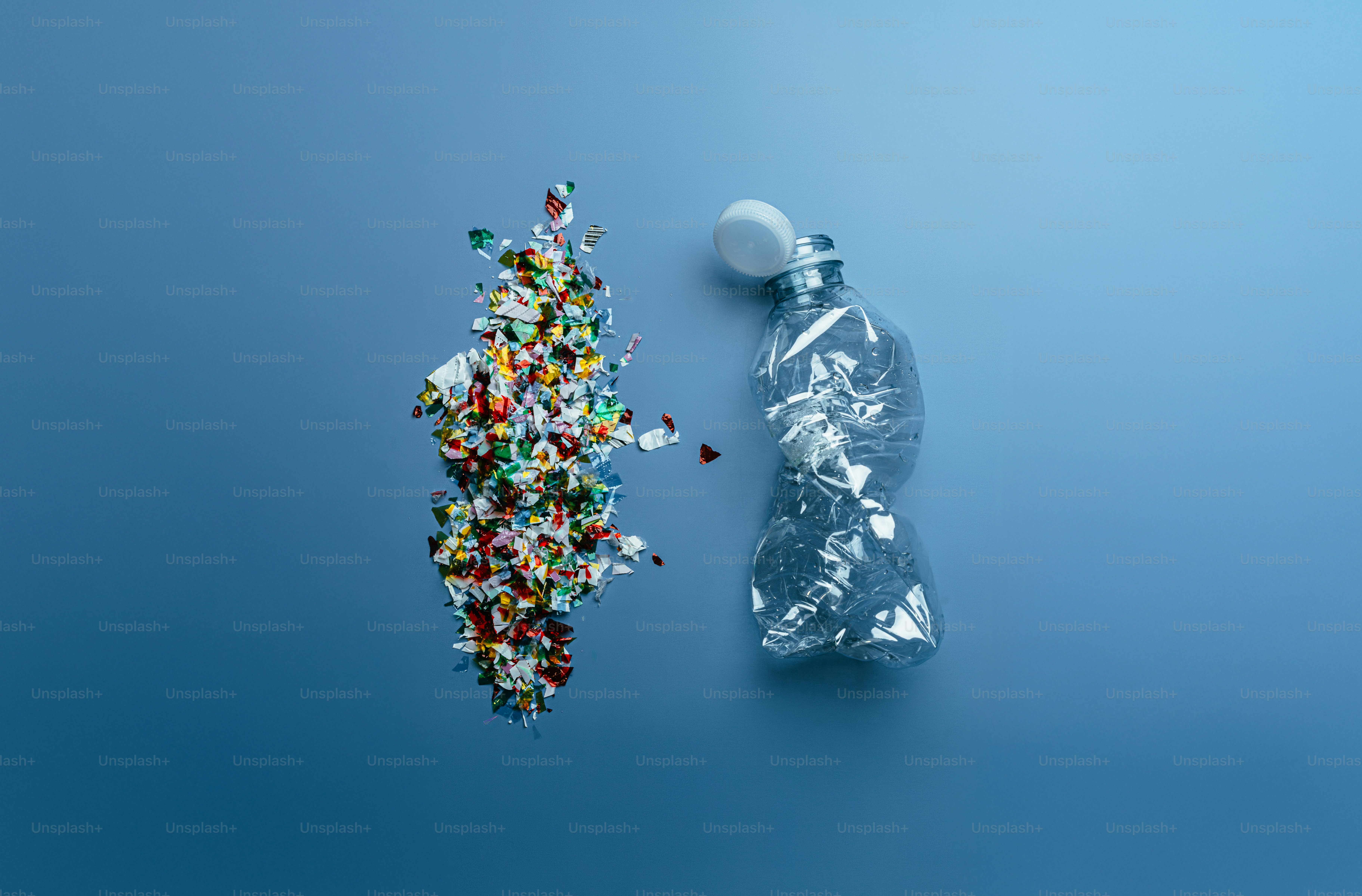 Plastic bottle broken into colorful microplastics on blue background