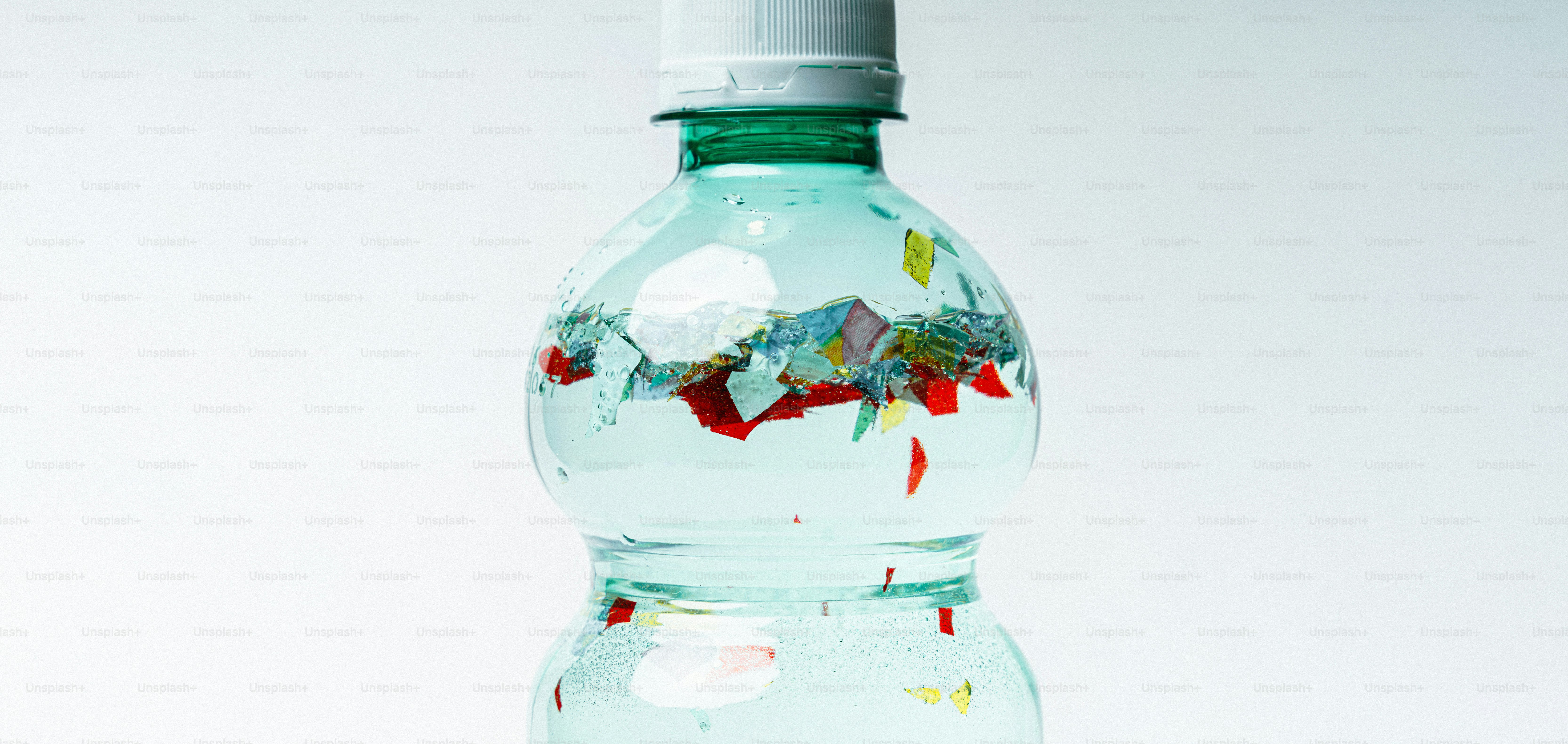Plastic bottle filled with colorful debris against white background