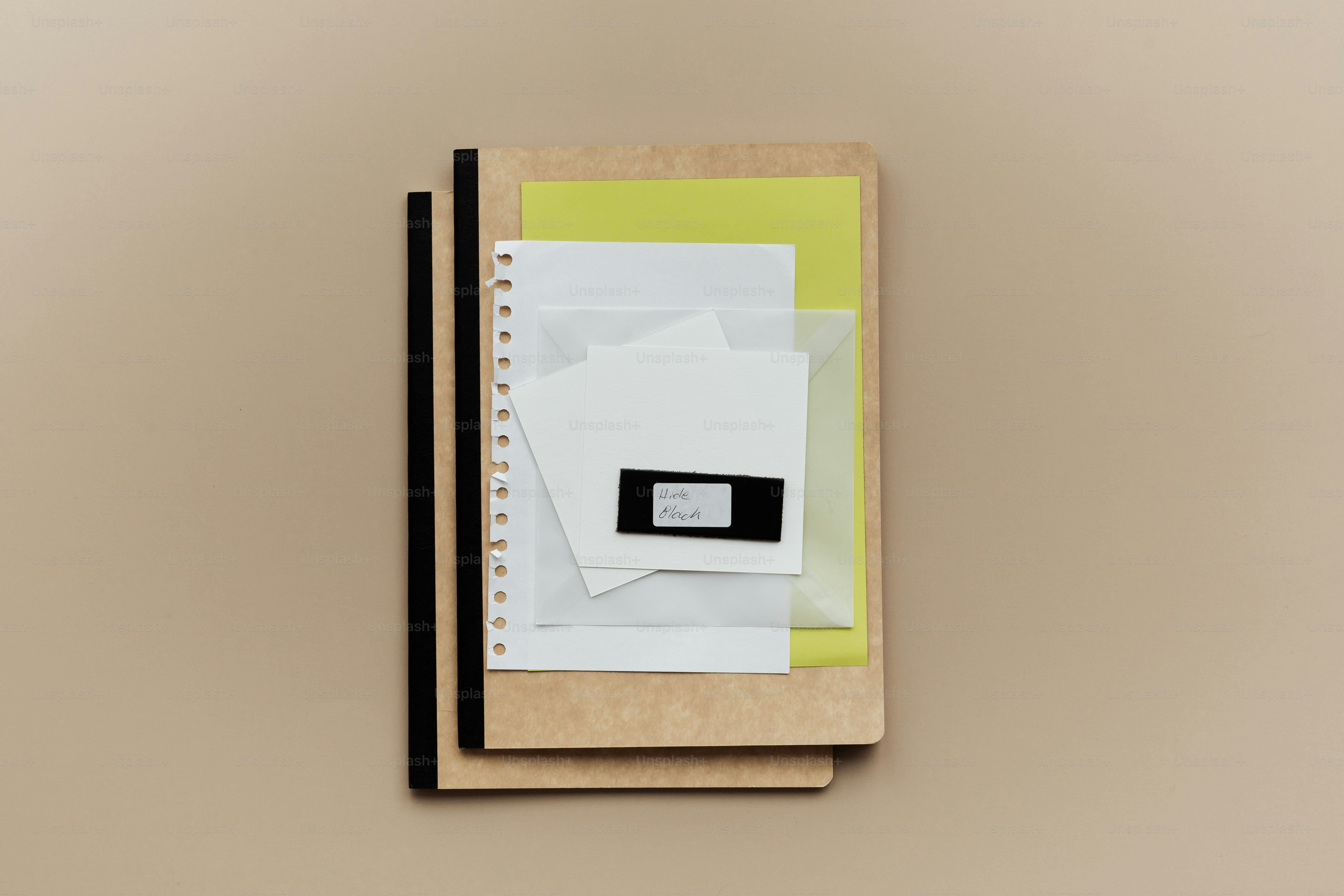 A stack of notebooks and papers on a tan surface.