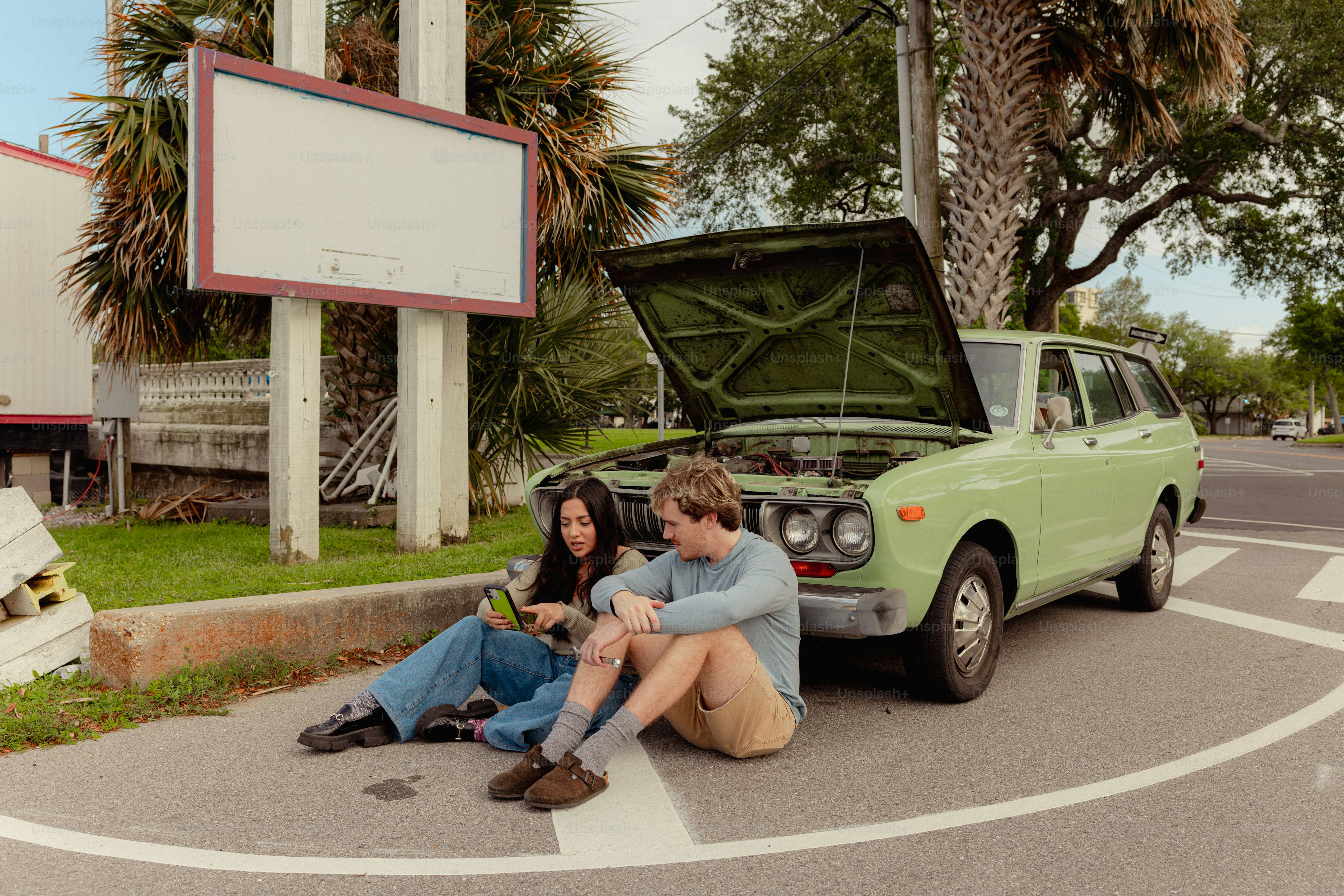 Pareja sentada junto a un coche averiado al borde de la carretera.