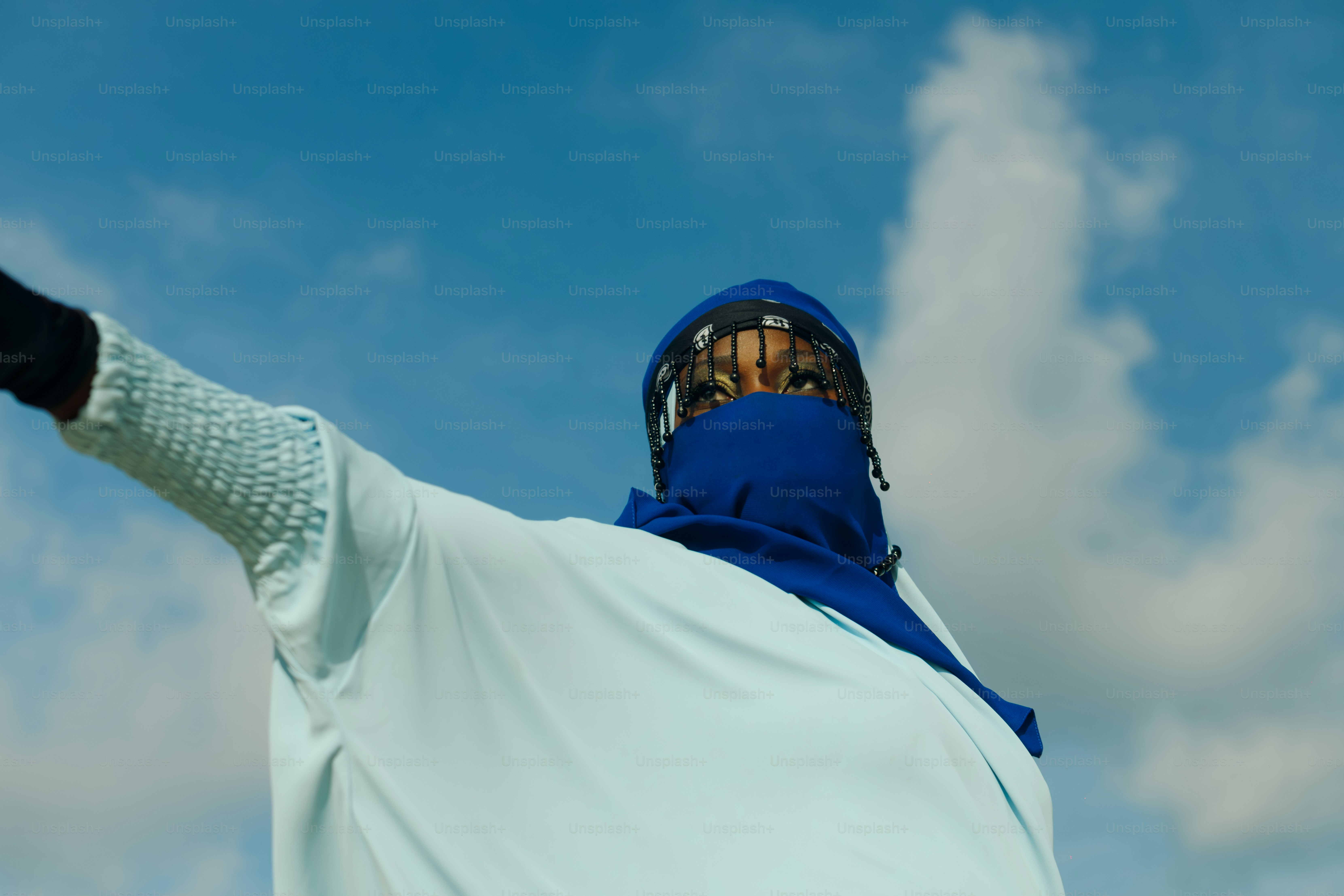 Femme en hijab bleu et chemise blanche, bras tendu