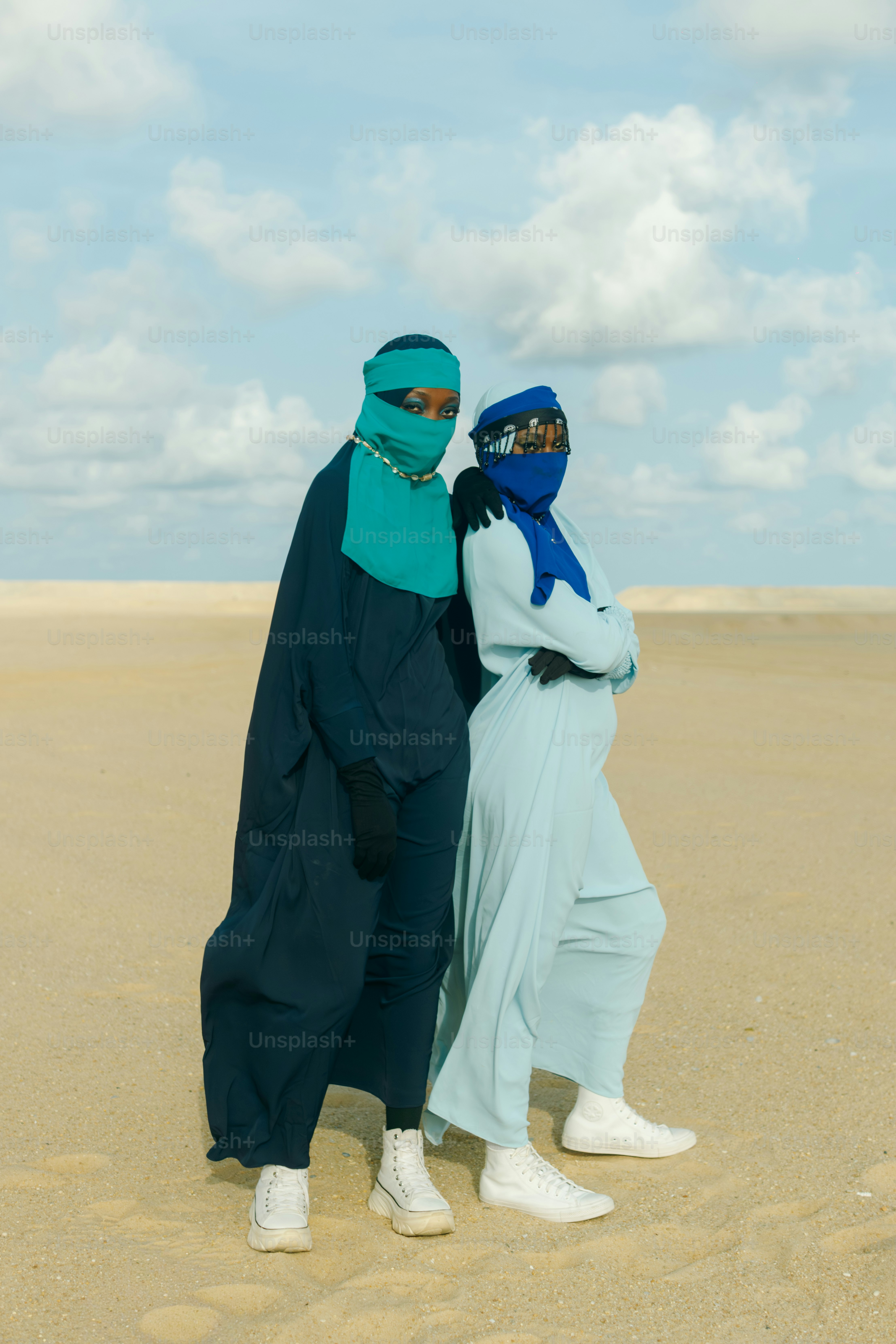 Deux femmes en tenue traditionnelle se tiennent sur un paysage sablonneux.