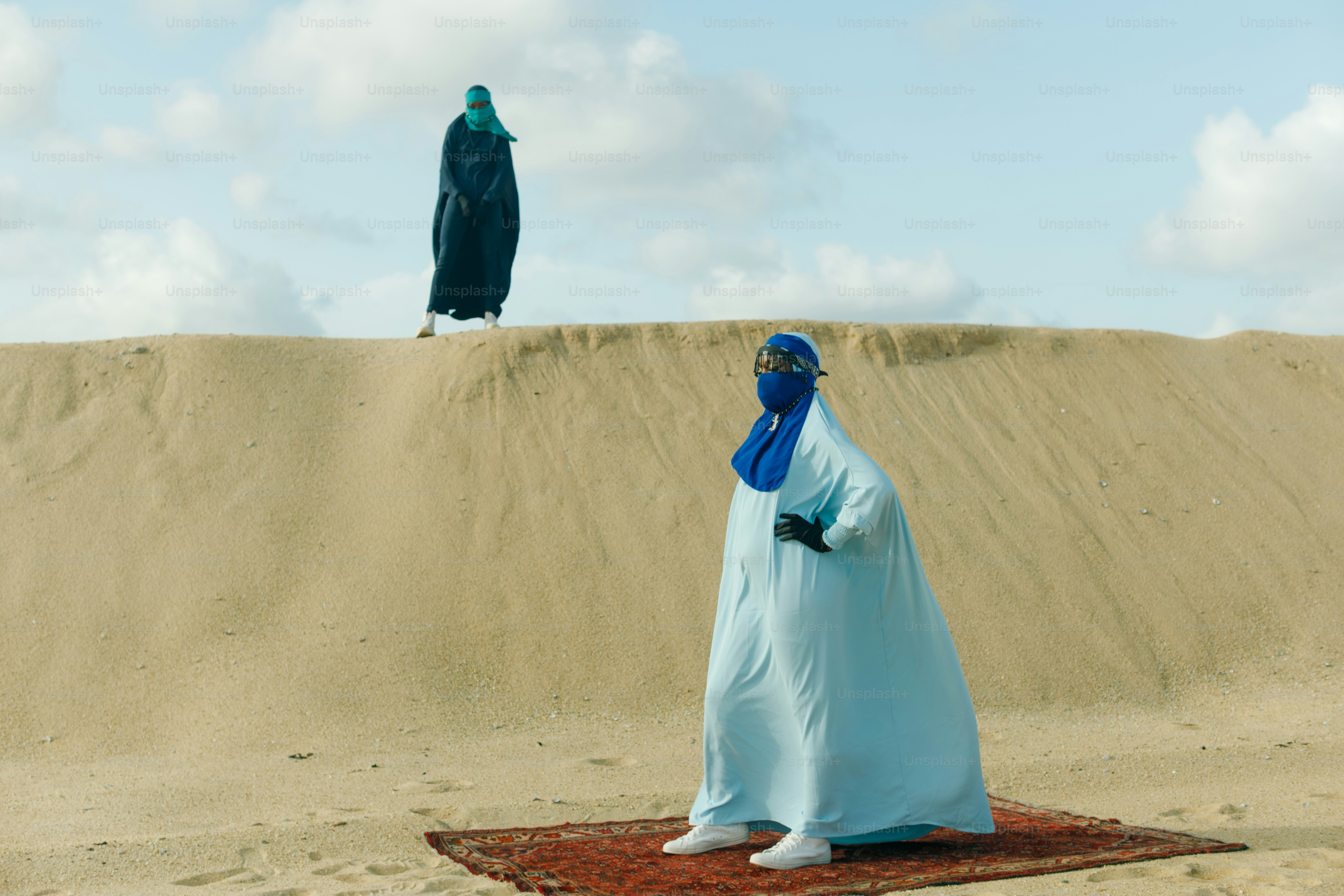 Deux personnes en burqa se tiennent sur une dune de sable.