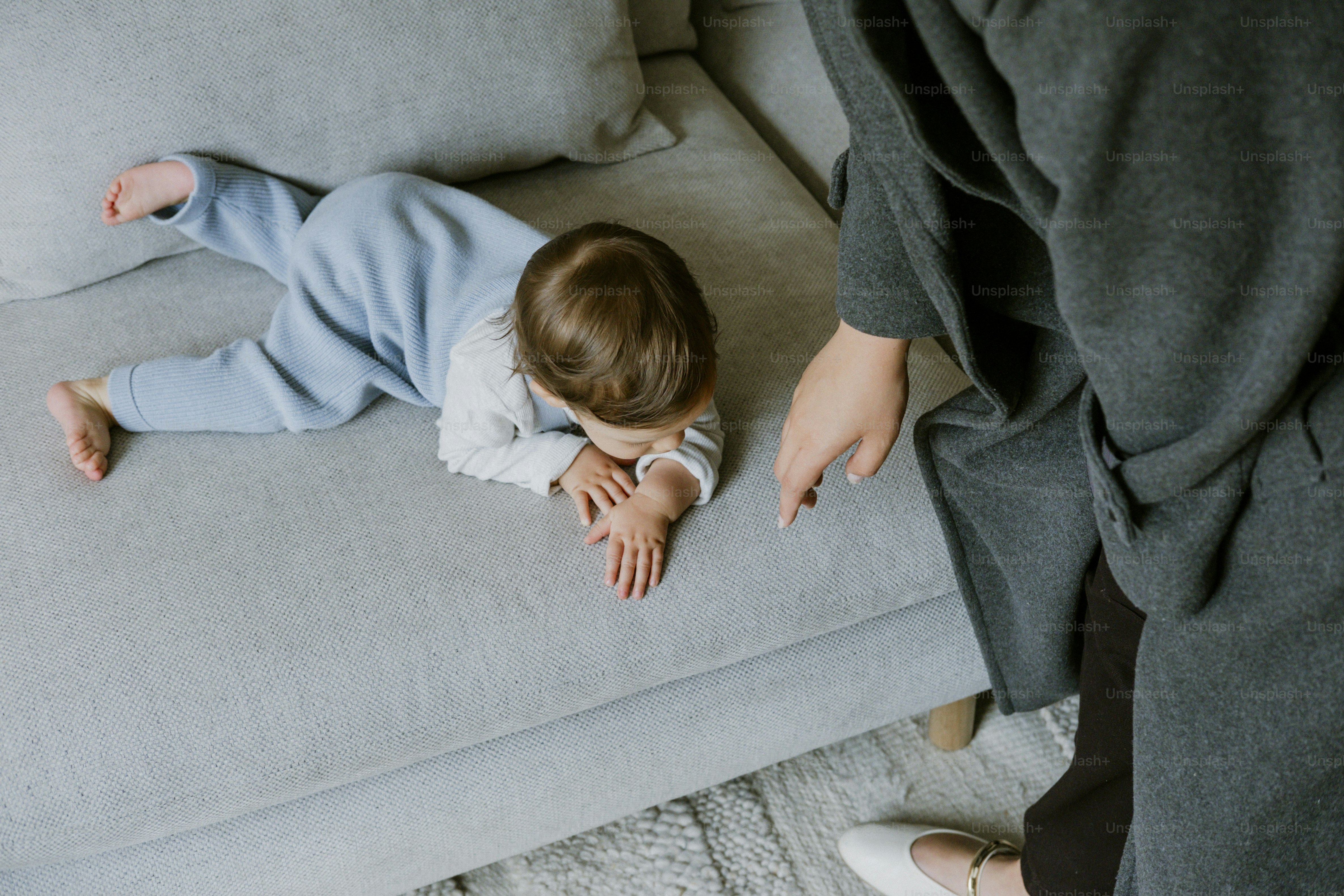 Baby lying on a couch near an adult.