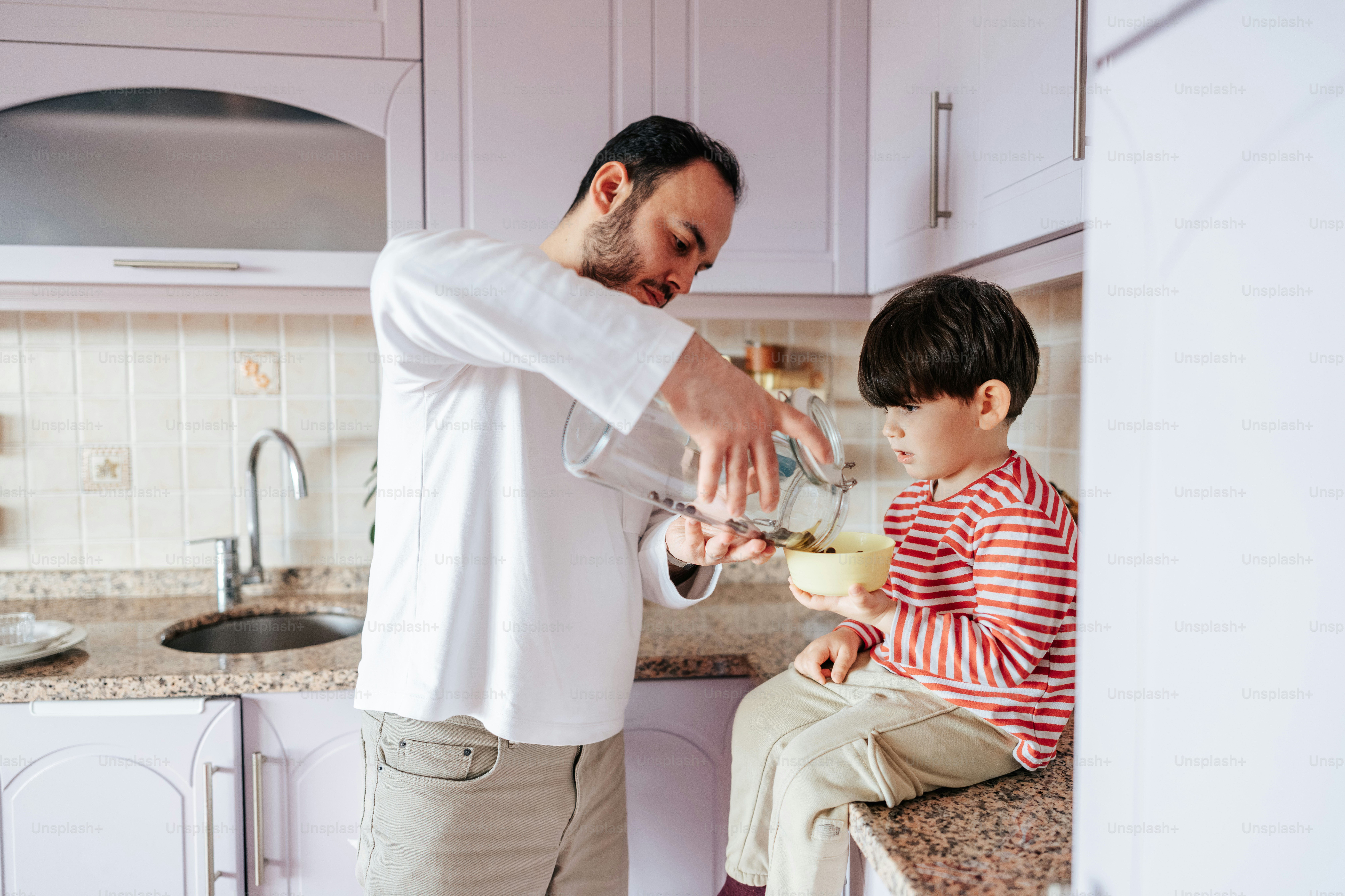 Ayah menuangkan air ke dalam mangkuk putra di dapur.