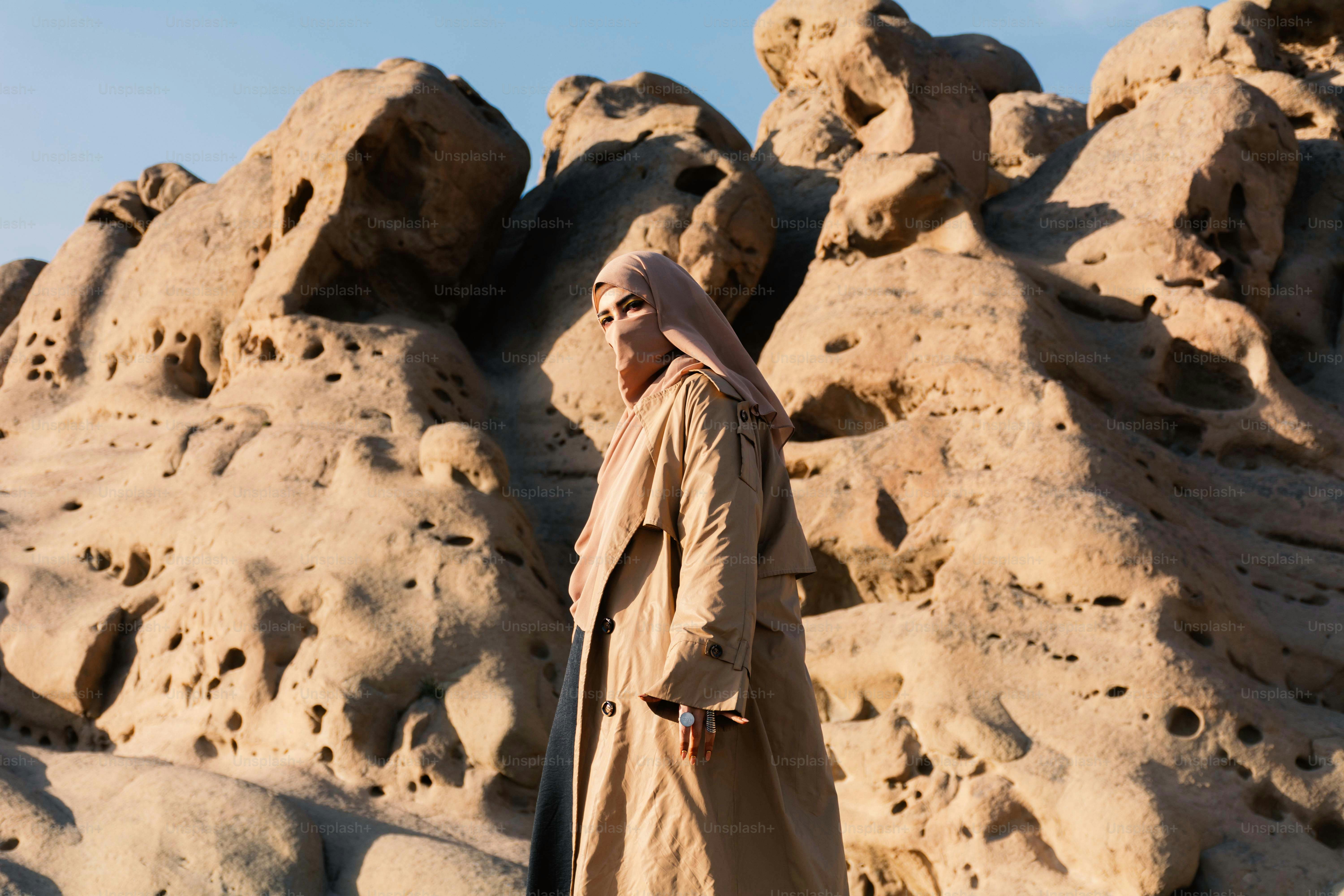 Une femme en manteau beige se tient contre des formations rocheuses.