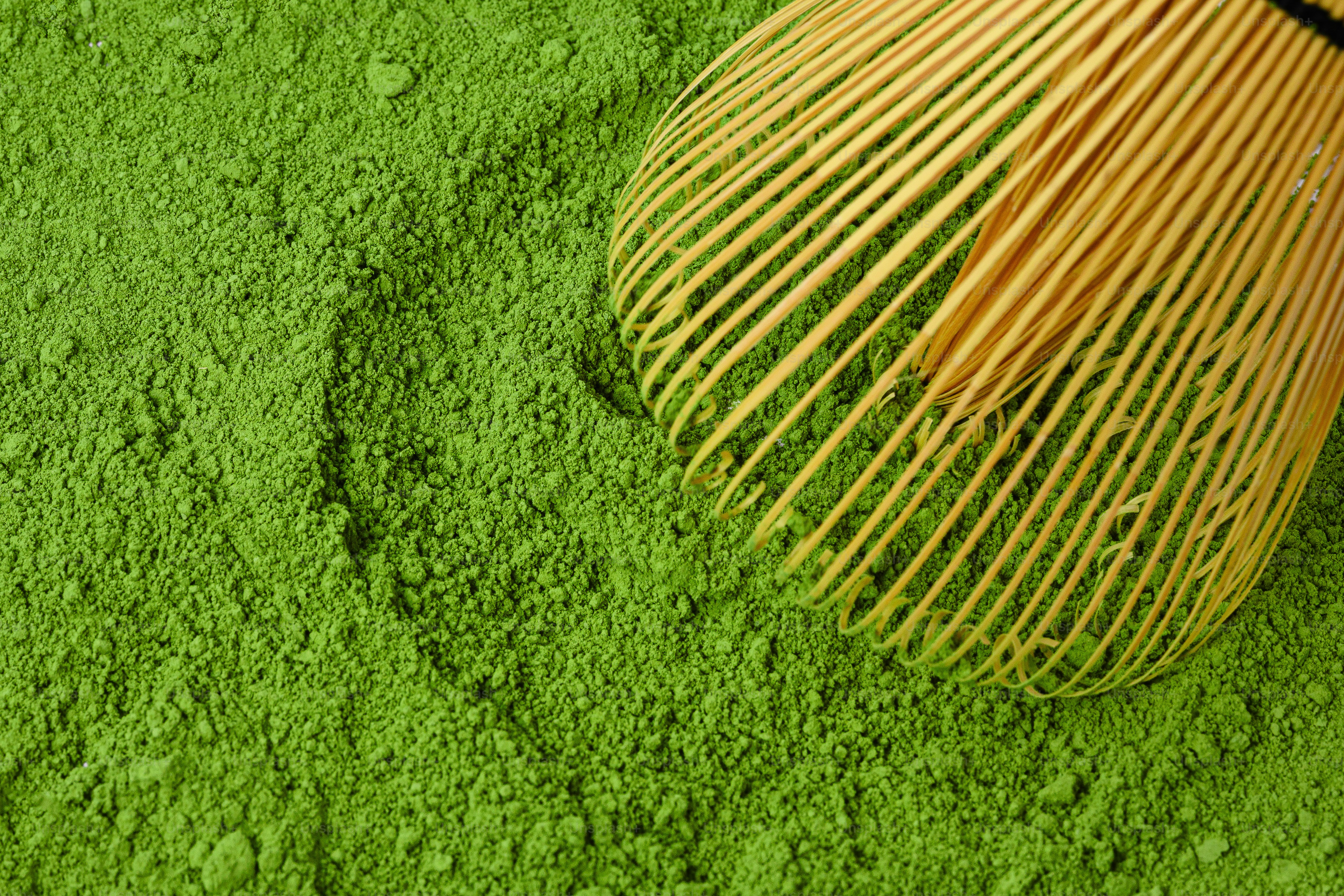 Una frusta di bambú si appoggia su polvere di matcha verde brillante.