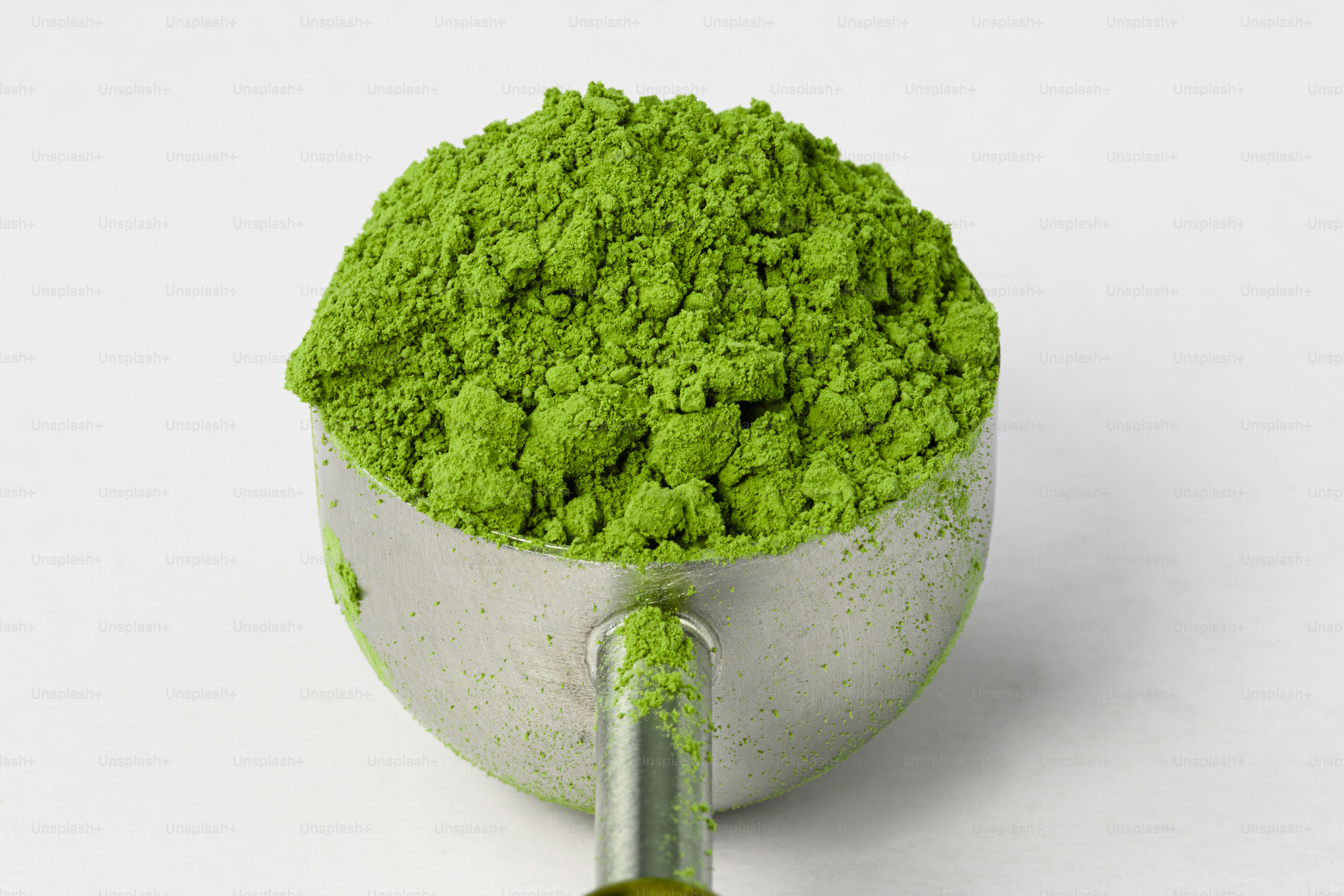 A metal scoop filled with vibrant green matcha powder.