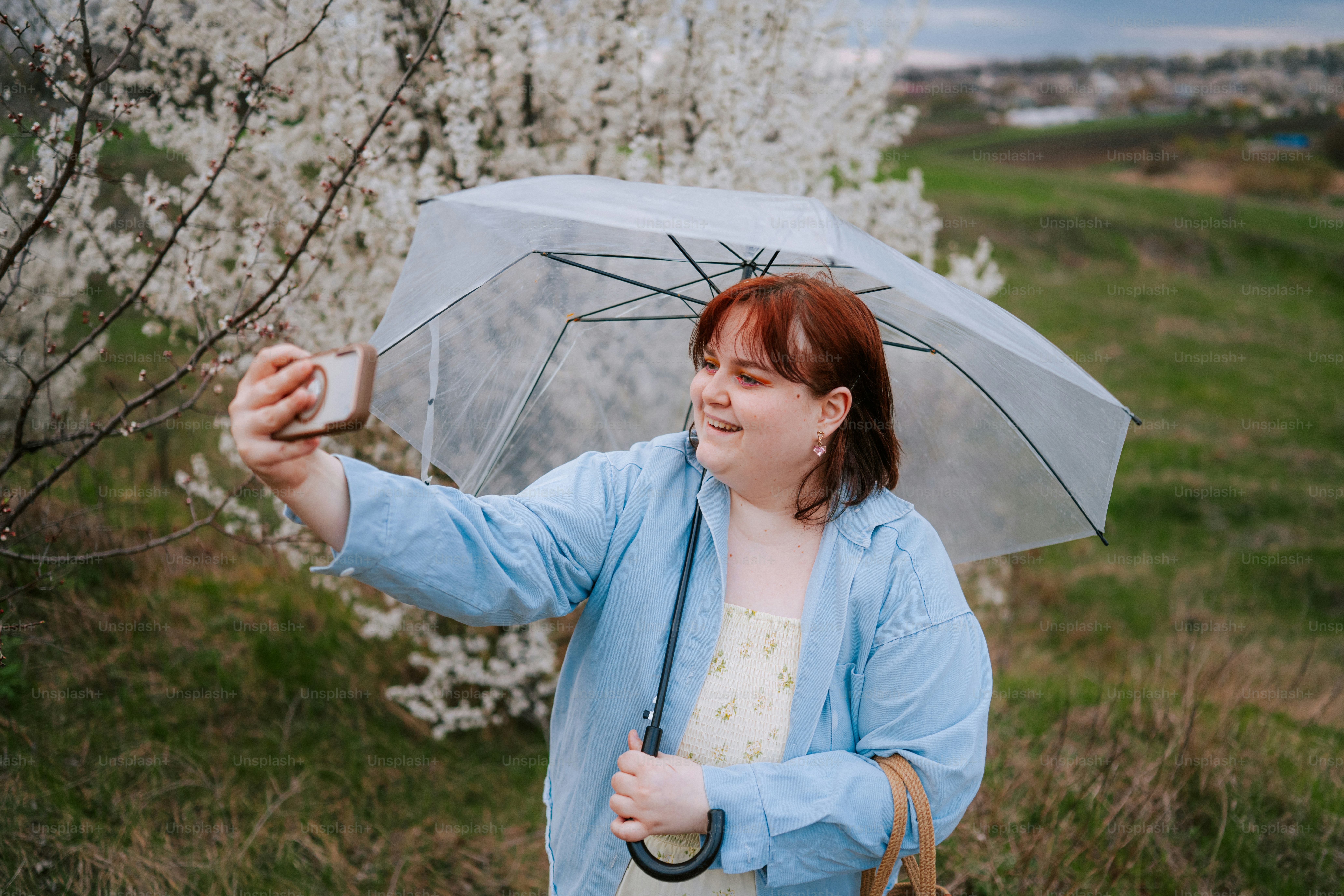 A woman takes a selfie with a clear umbrella outdoors.