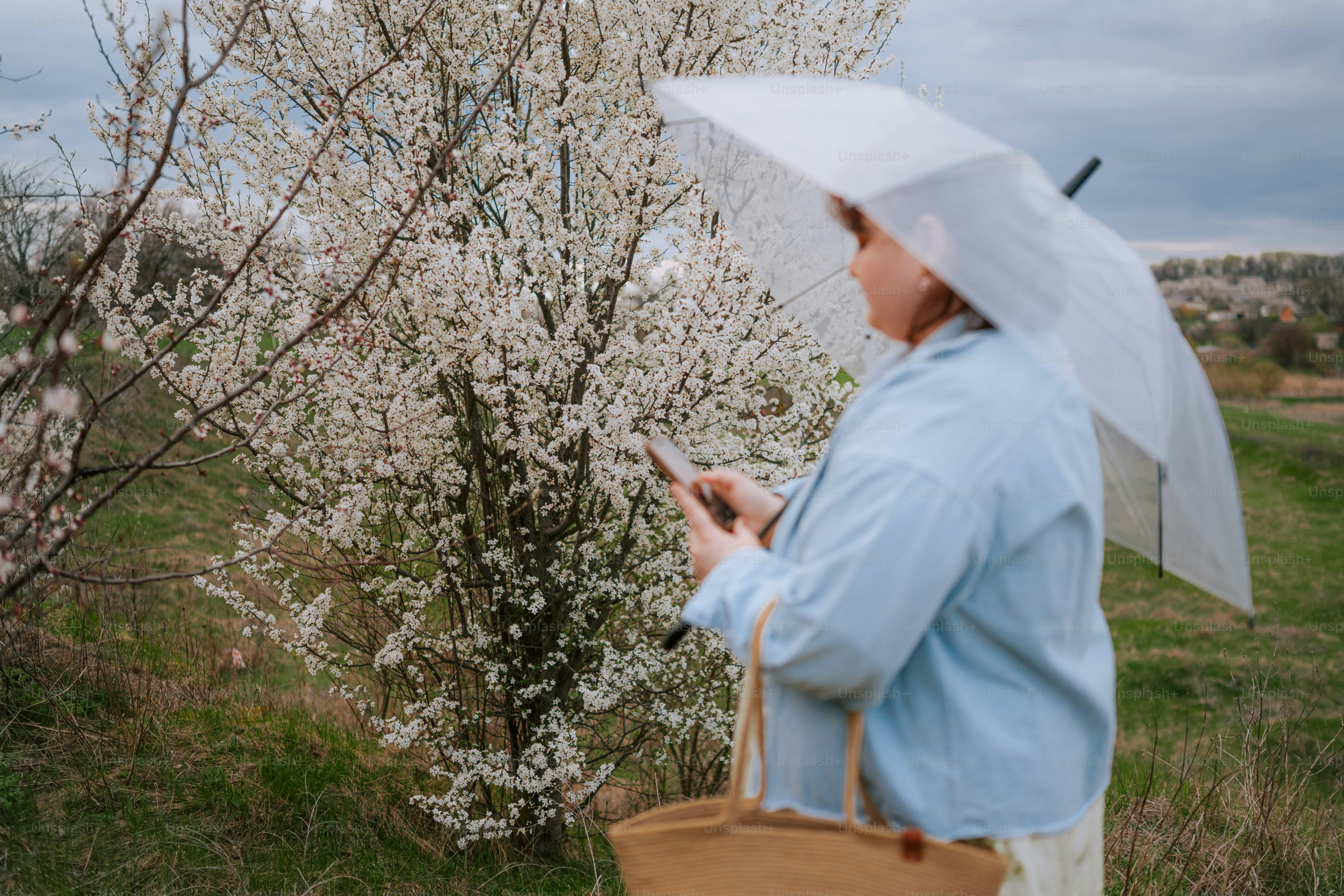 Woman with umbrella and phone near blooming tree