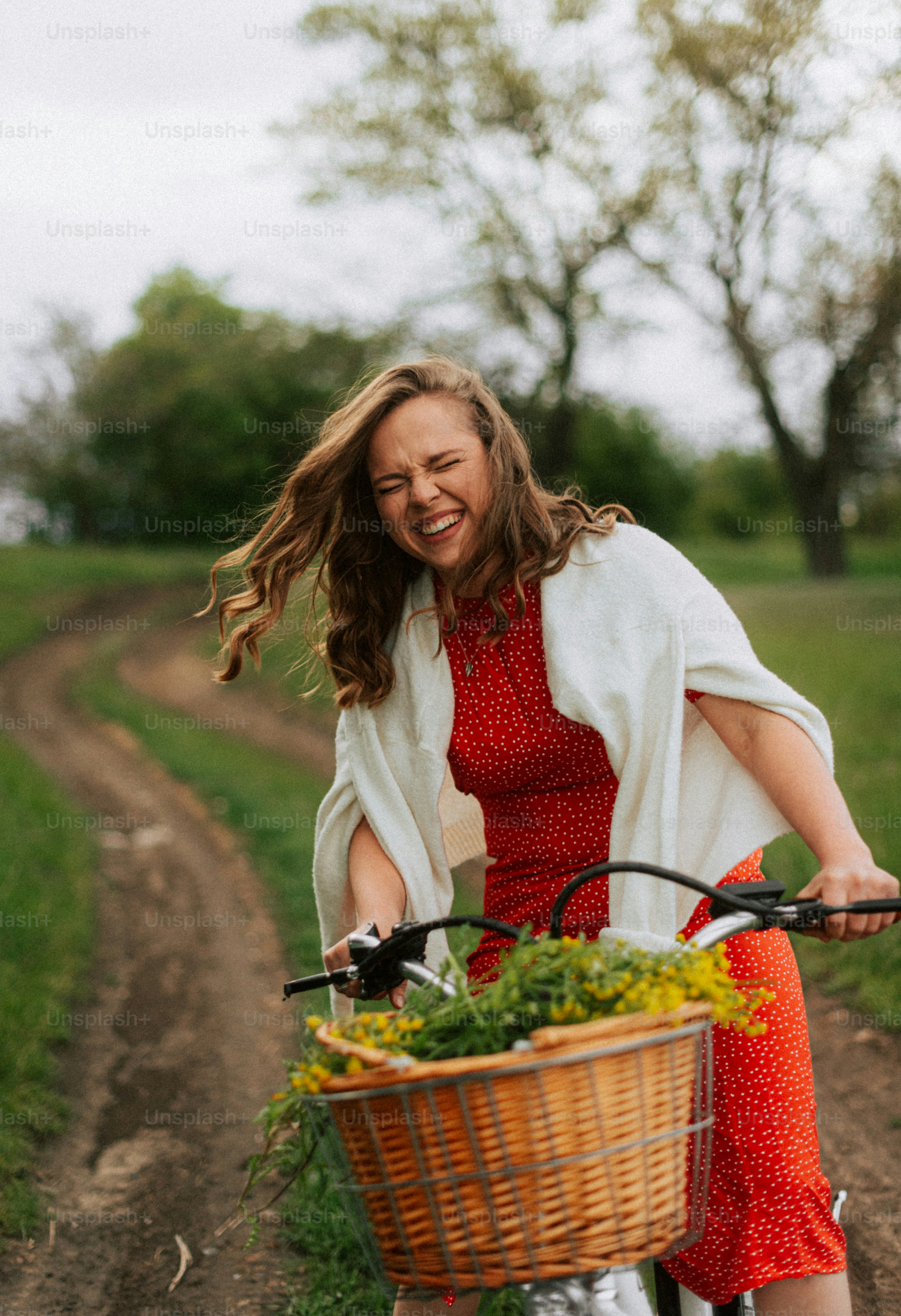 A laughing woman in a red dress rides a bicycle.