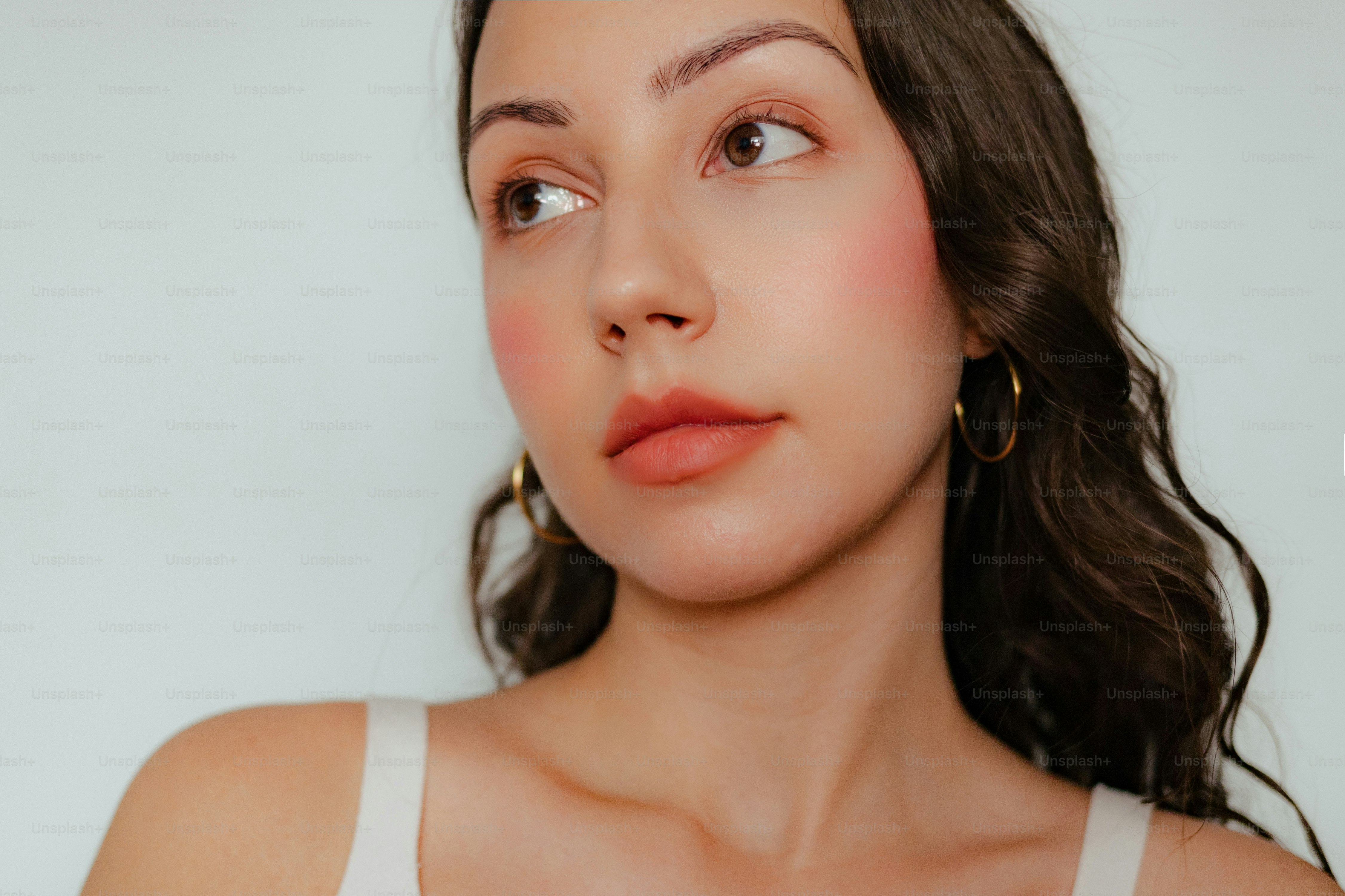 Une jeune femme aux cheveux foncés ondulés et aux boucles d’oreilles en cerceau.