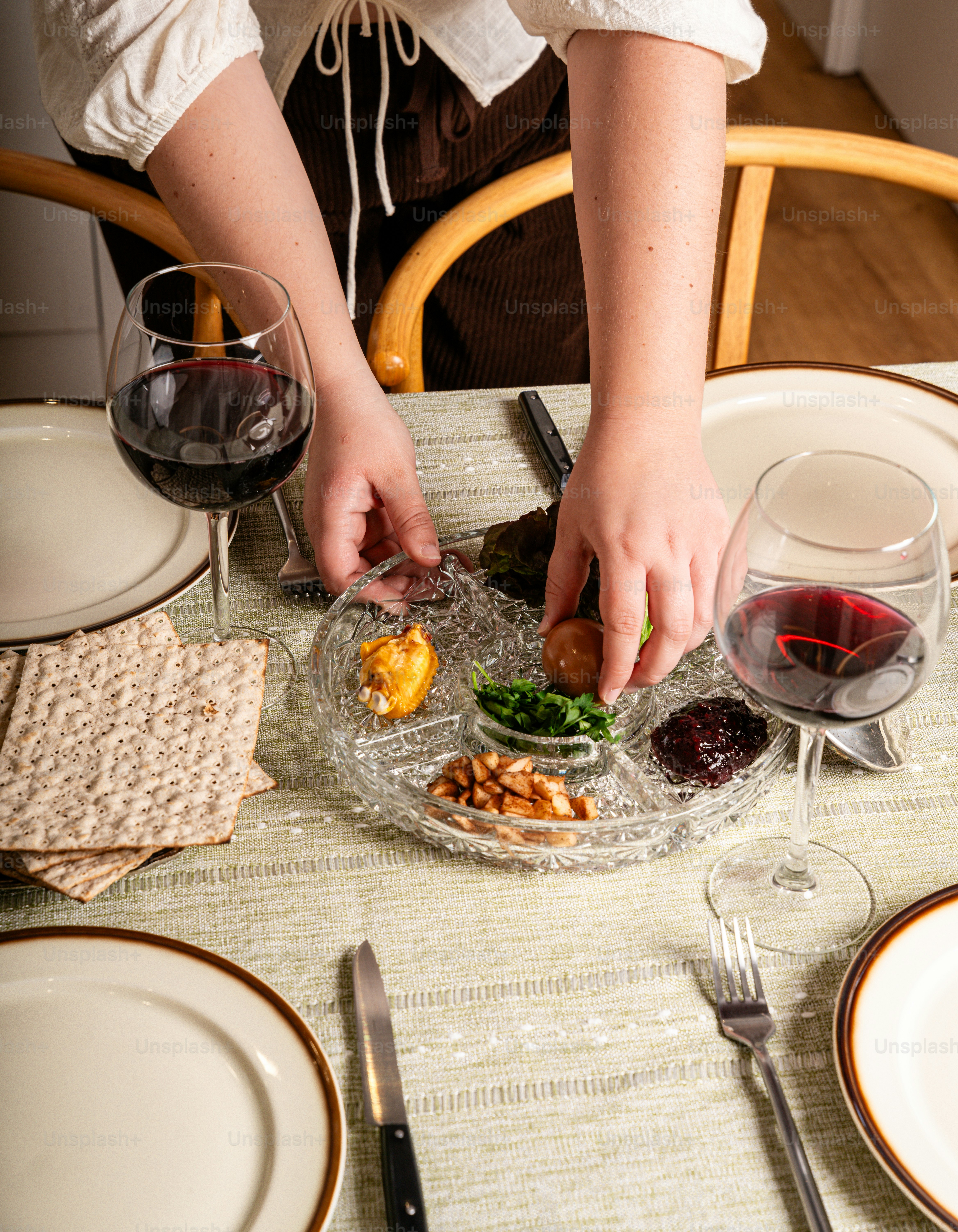 Le mani che sistemano un piatto del seder con matzah e vino