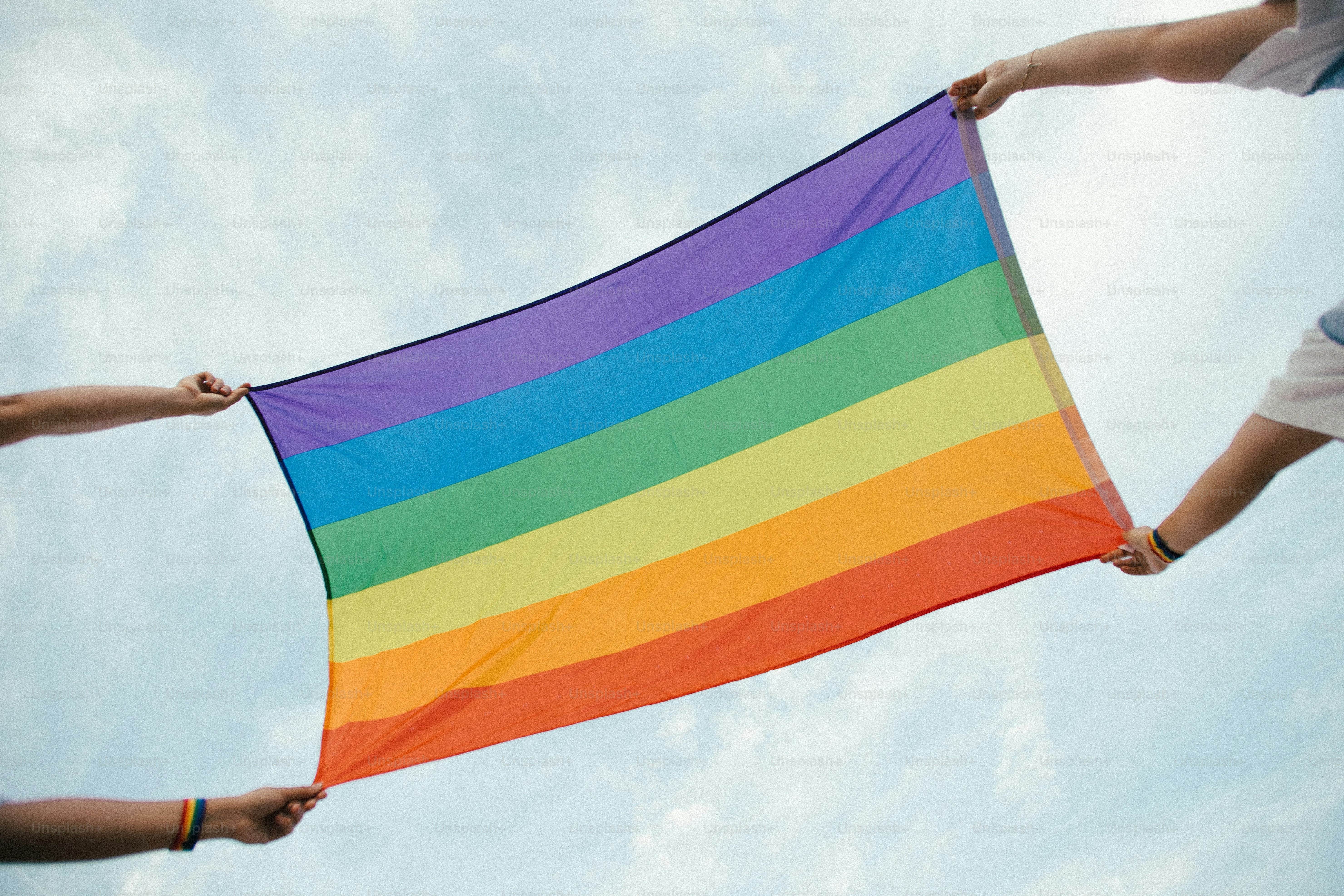 Deux mains tenant un drapeau arc-en-ciel contre le ciel.