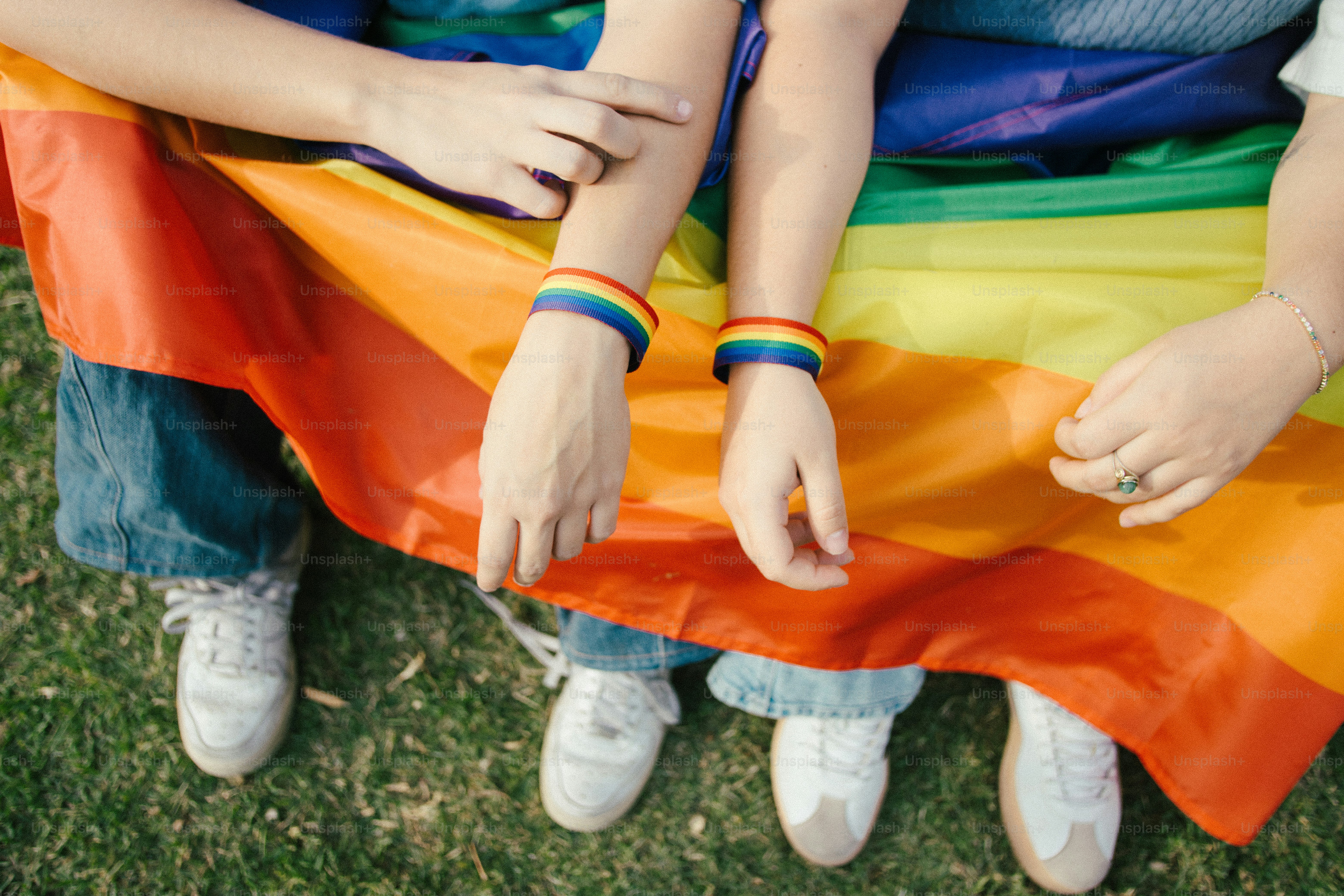 Des gens portant des bracelets arc-en-ciel sur un drapeau arc-en-ciel.